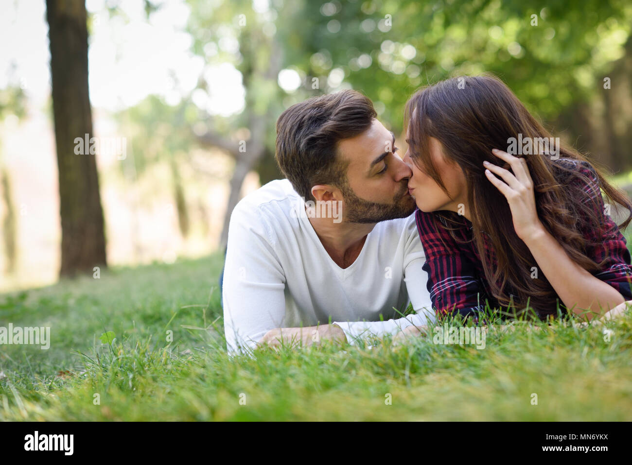 Beautiful young couple kissing on grass in an urban park. Caucasian man and  woman wearing casual clothes Stock Photo - Alamy