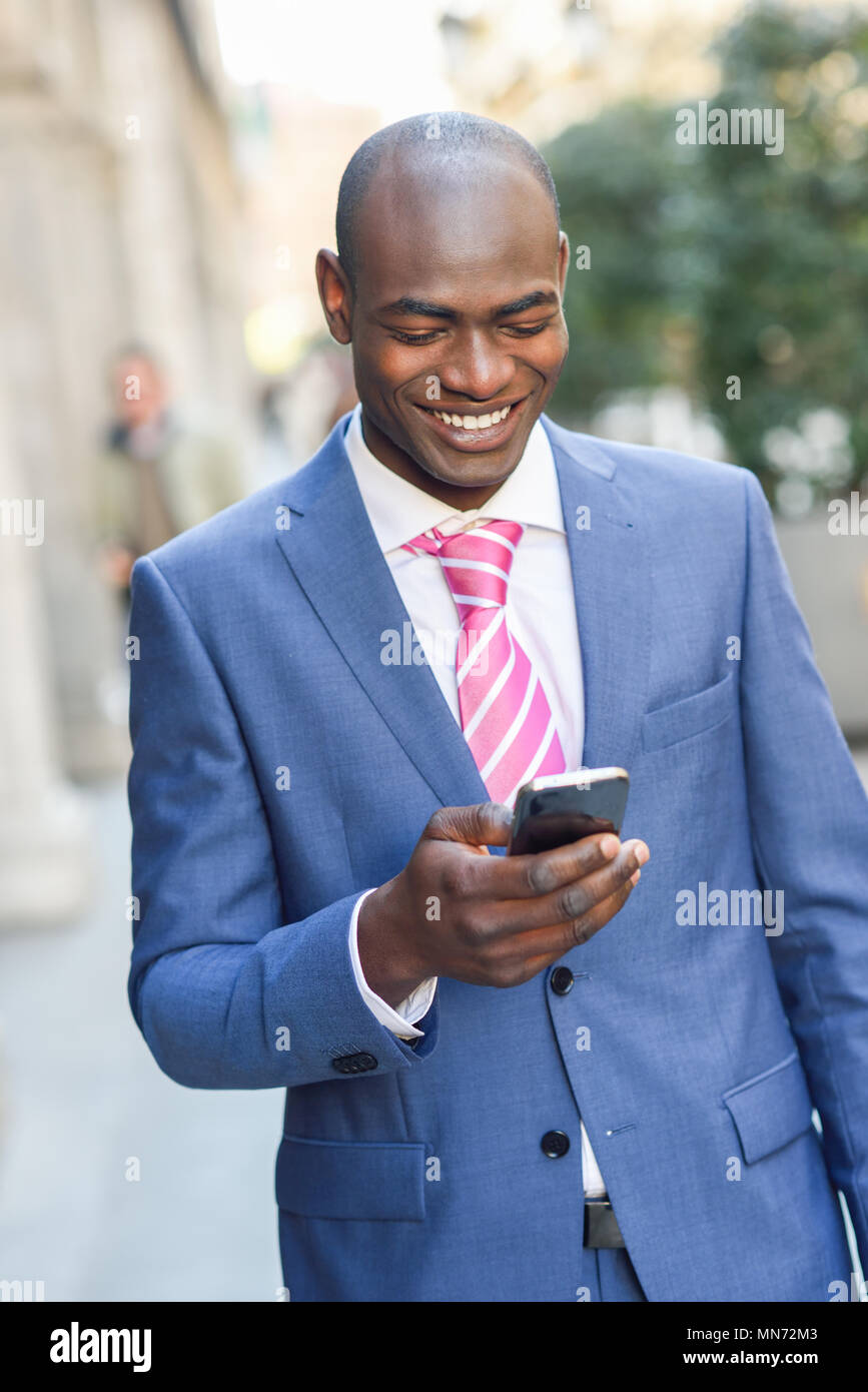 Portrait of a black businessman wearing suit reading his smart phone in ...