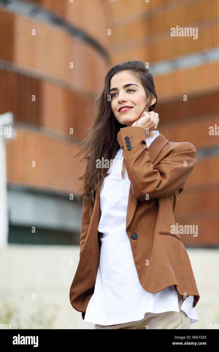 Young woman with nice hair standing outside of office building.  Businesswoman wearing formal wear with wavy hairstyle. Young girl with  brown jacket and trousers Stock Photo - Alamy