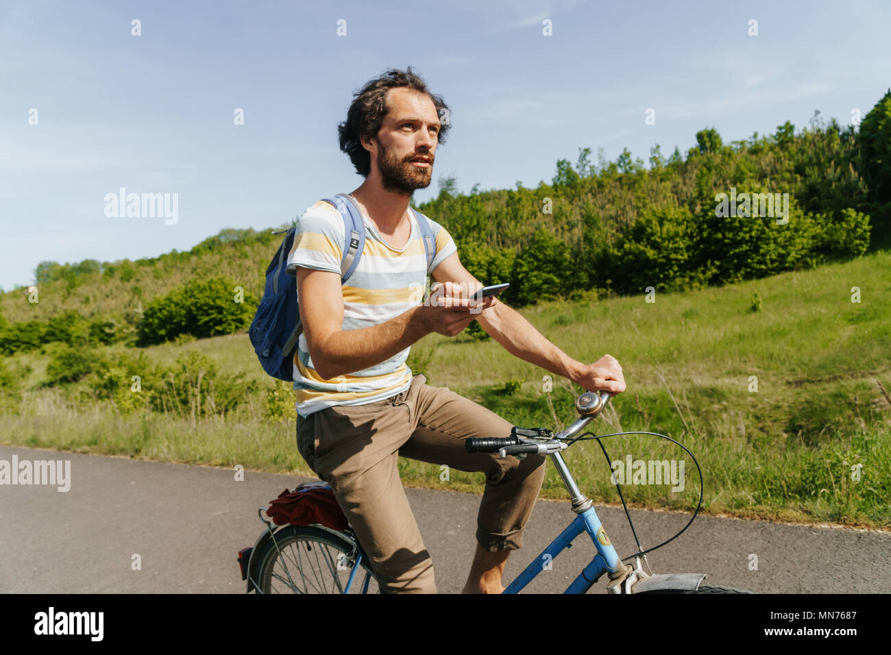 young caucasian man biking through the nature with smartphone in his hands to navigate Stock Photo