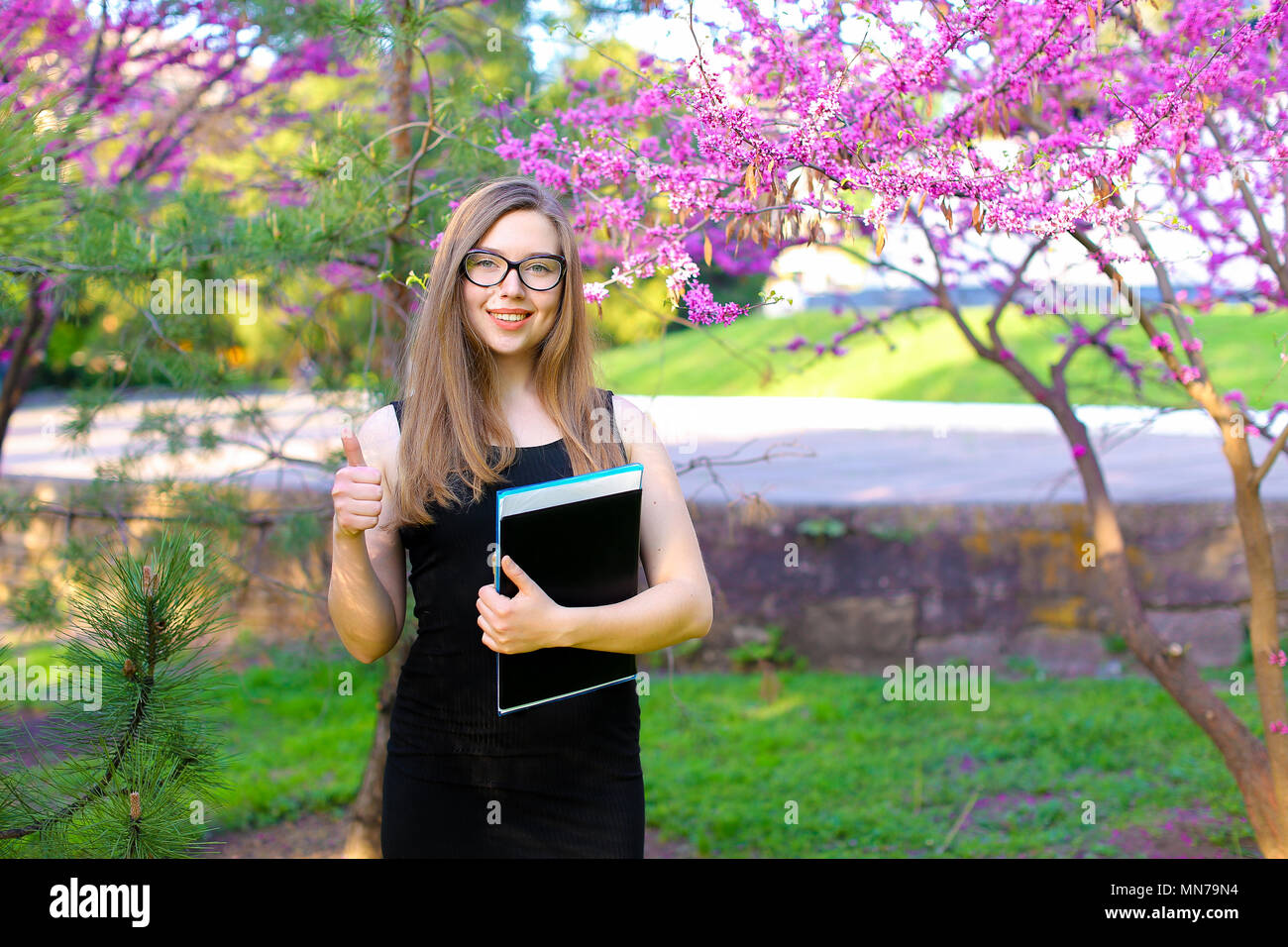 Charming female student showing thumbs up in garden with documents in ...