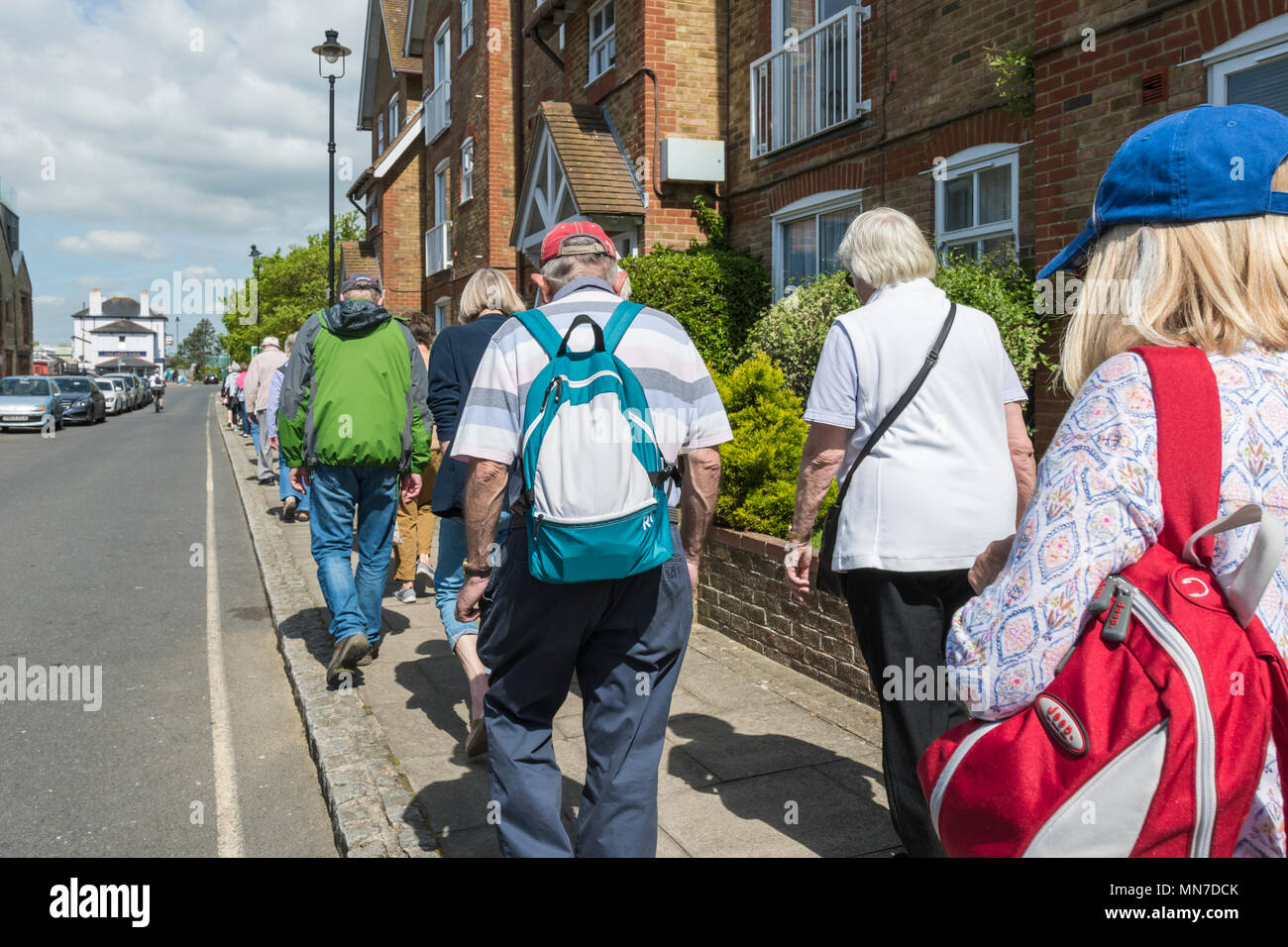 Group of elderly people with backpacks walking along a narrow pavement in the UK. Stock Photo