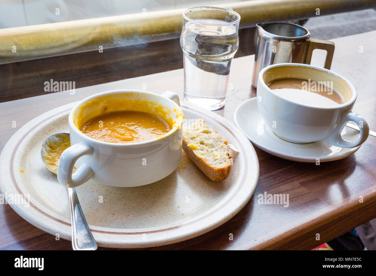Half eaten bowl of vegetable soup with coffee, water, bread and spoon on cafe counter Stock Photo