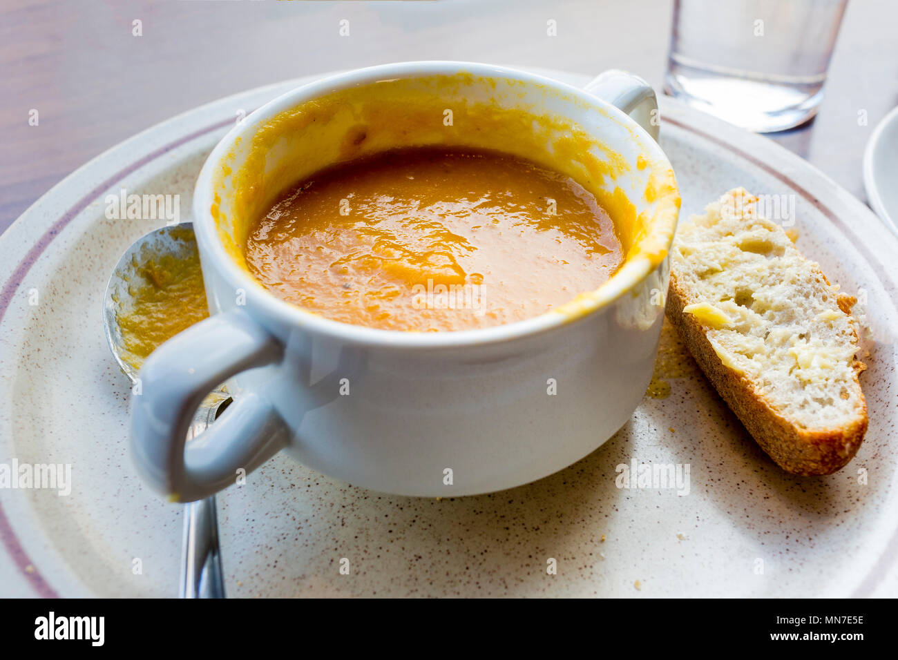 Half eaten bowl of vegetable soup with bread and spoon on cafe counter Stock Photo