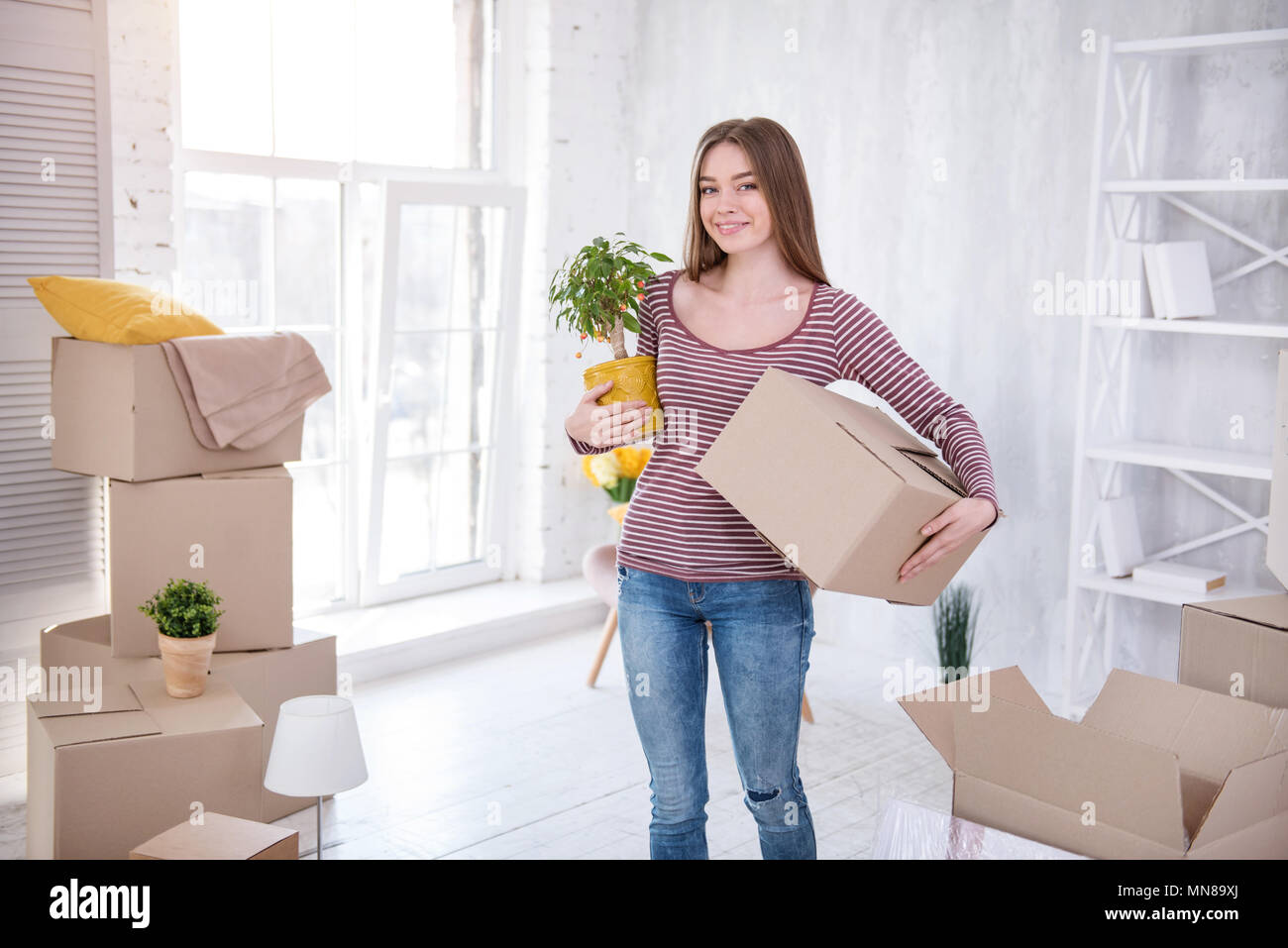 Cheerful young woman posing with plant and box Stock Photo