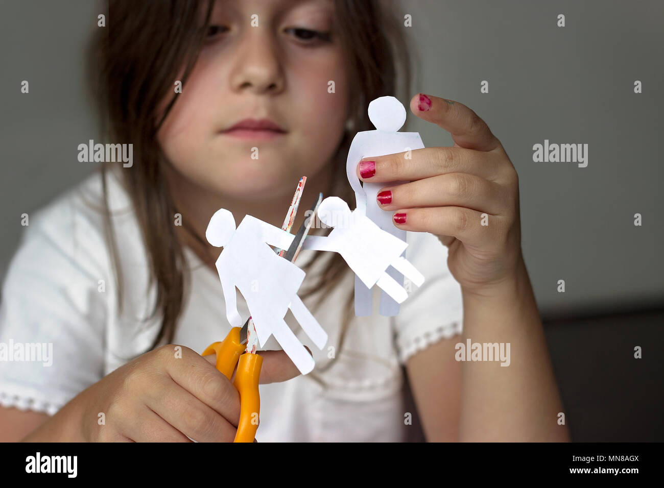 Sad little girl with paper family and scissors; divorce or family problems concept Stock Photo