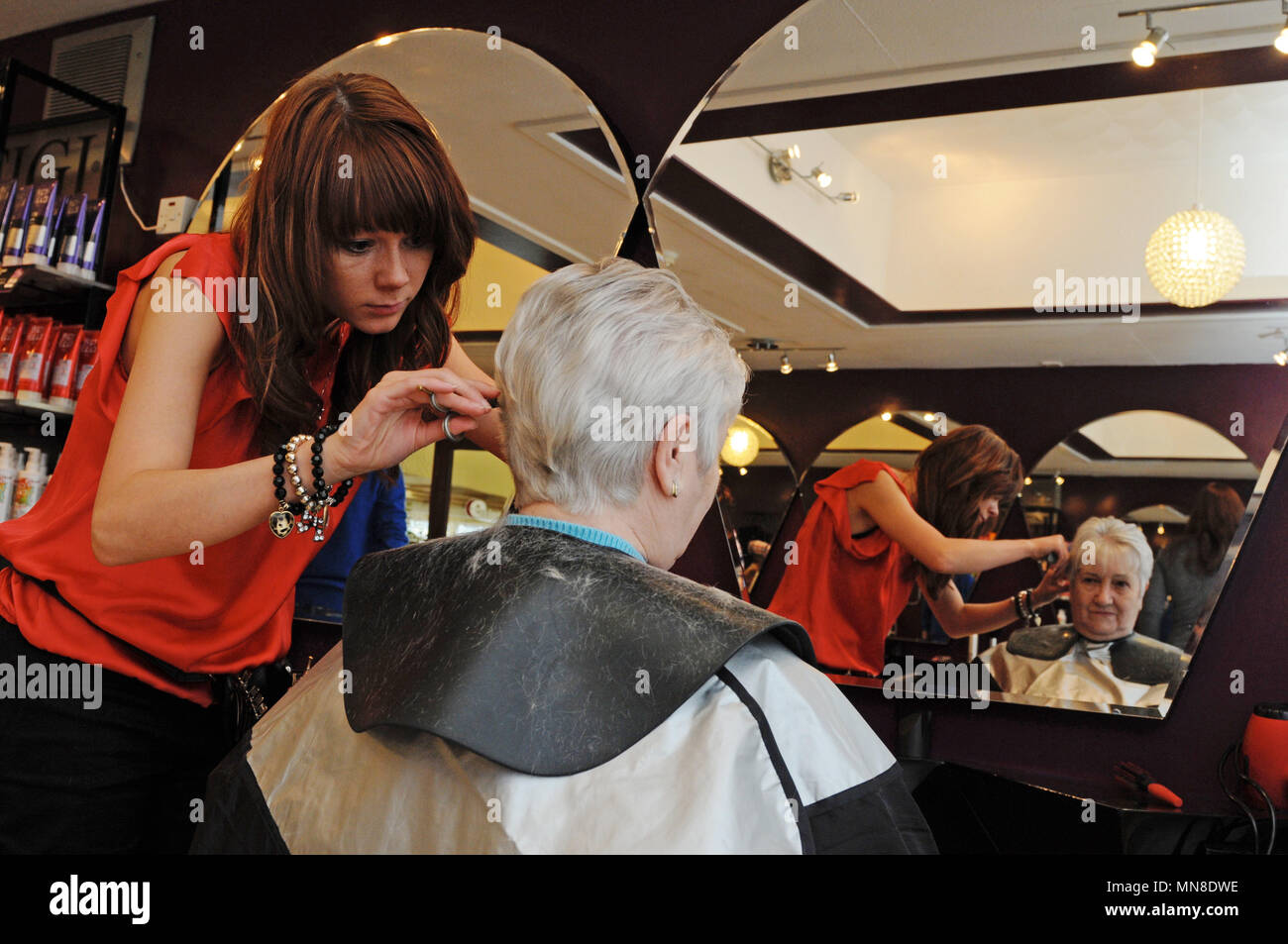 young hairdresser cutting elderly old ladies hair in modern hair salon Stock Photo