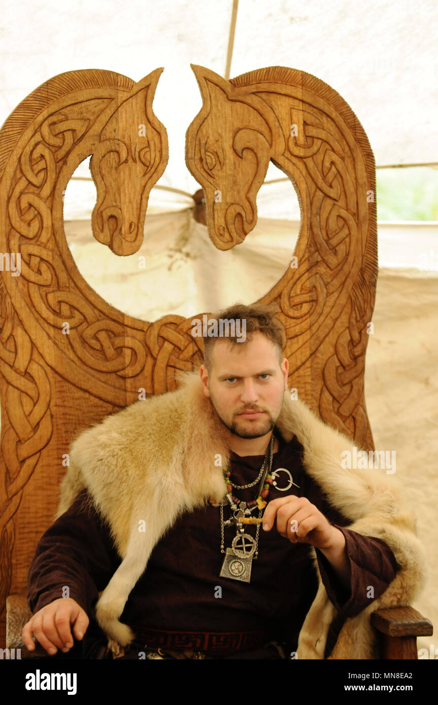Viking sat in ornate wooden chair wearing animal skin Stock Photo