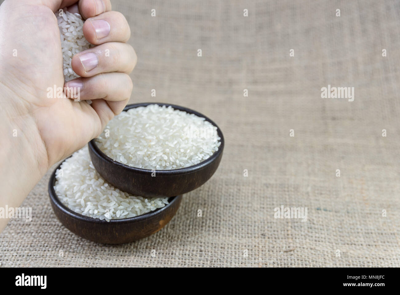 man hand putting rice in wooden bowl on sackcloth background Stock