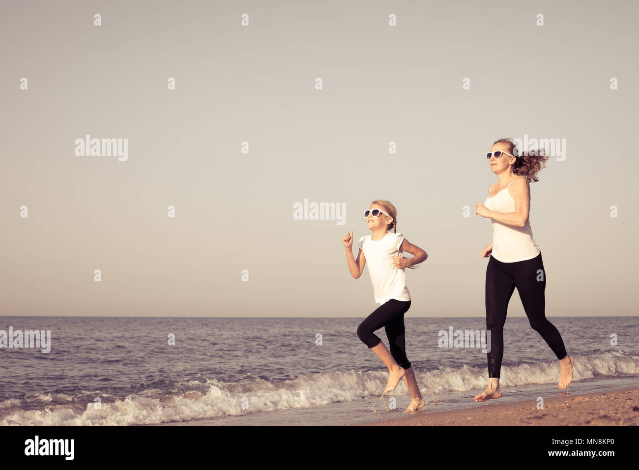 Mother and daughter running on the beach at the day time. People having fun outdoors. Concept of summer vacation and friendly family. Stock Photo