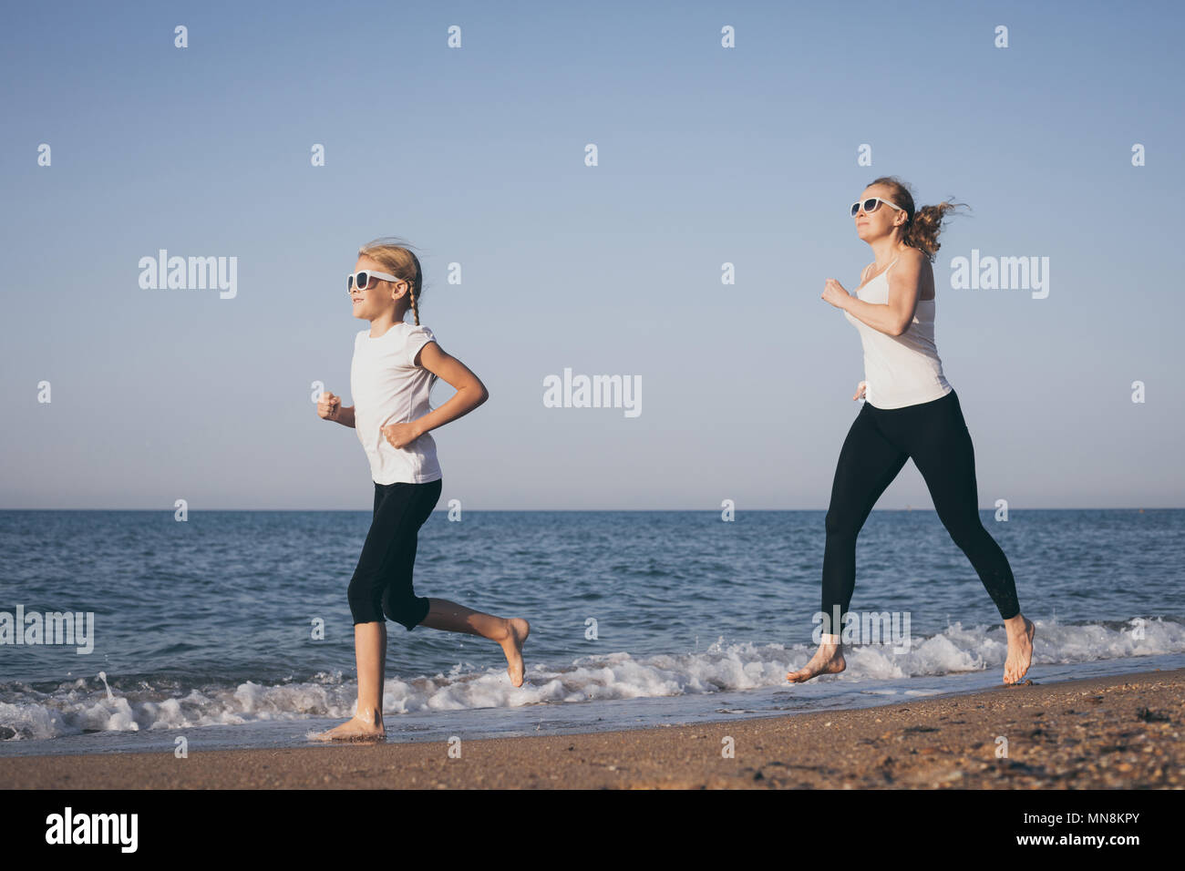 Mother and daughter running on the beach at the day time. People having fun outdoors. Concept of summer vacation and friendly family. Stock Photo