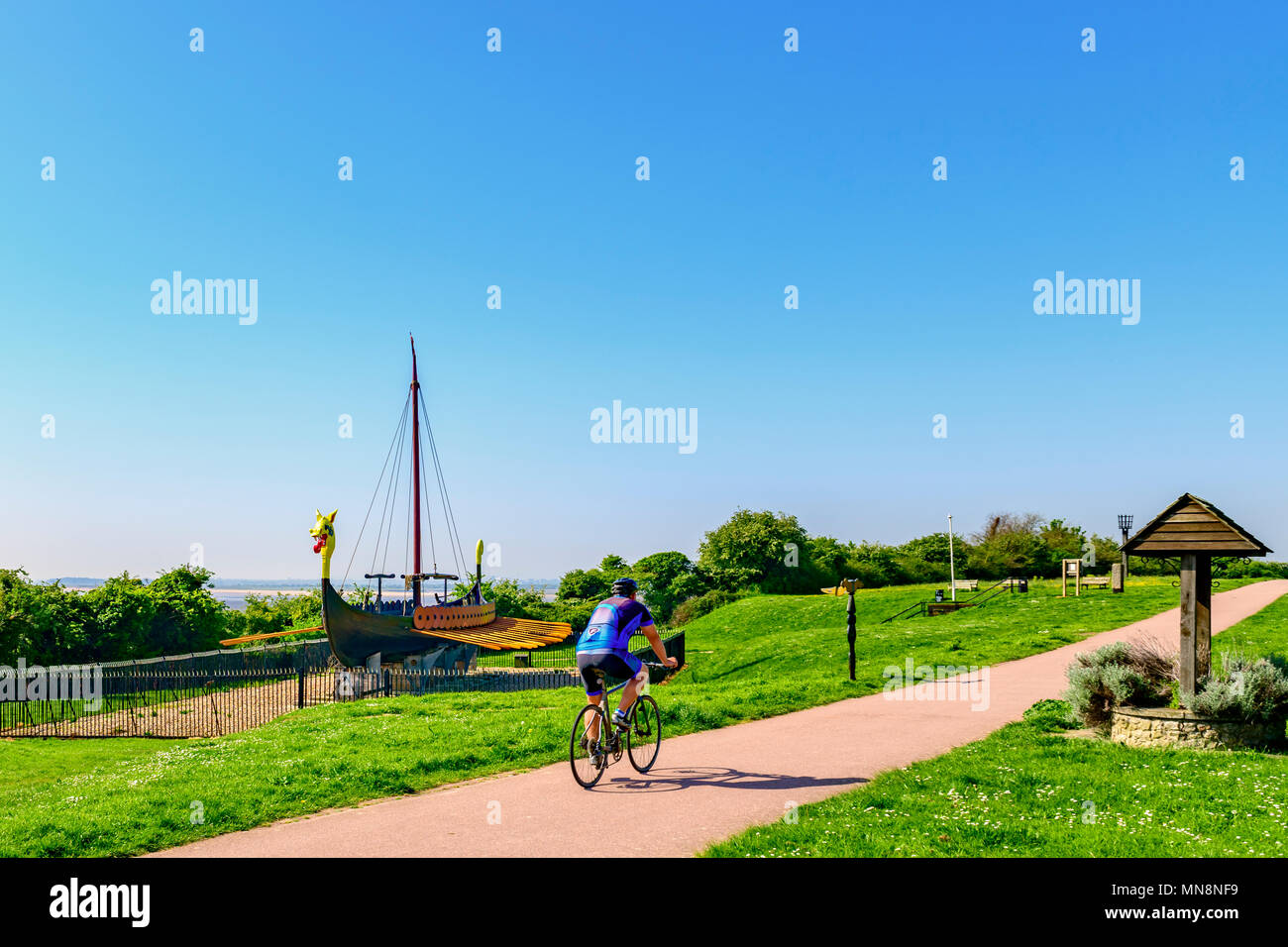 Cyclist passing in front of the Hugin, a replica viking ship at Cliffsend near Ramsgate UK Stock Photo