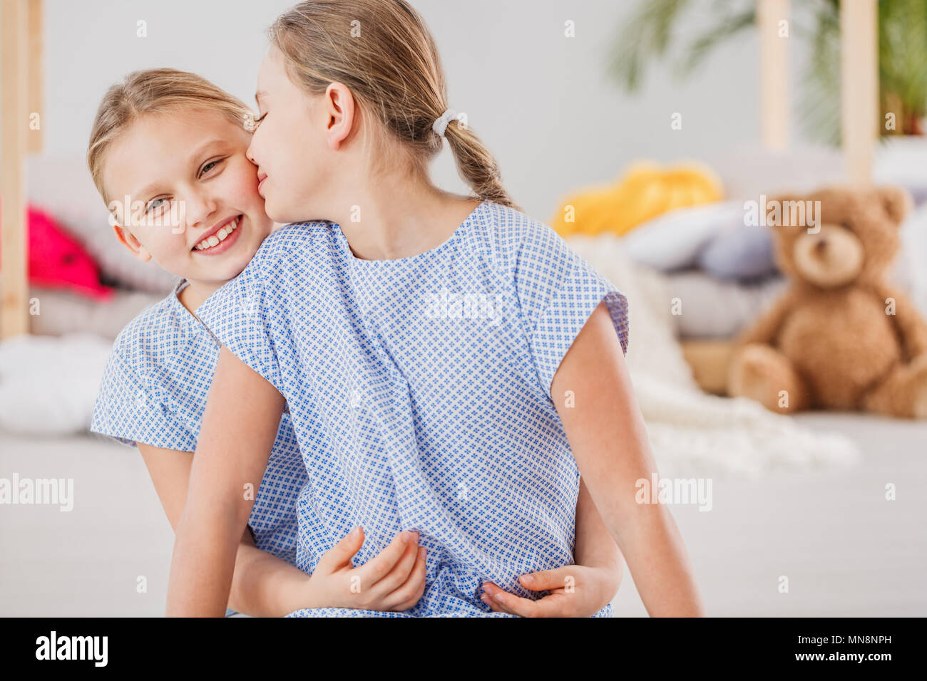 Two loving sisters wearing blue dresses hugging each other Stock Photo