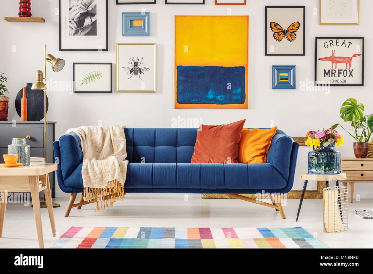 Navy blue couch with bright blanket and two cushions standing in white  living room interior with fresh flowers, gold lamp and gallery on the wall  Stock Photo - Alamy