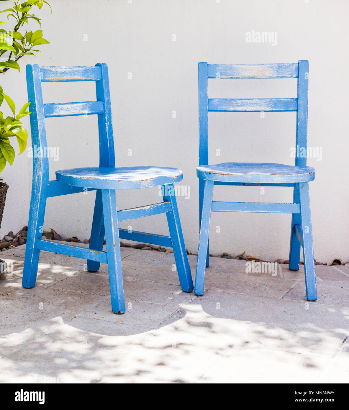 small weathered blue chairs. Painted and made to look distressed. Setting resembles a mediterranean garden, white walls and a travertine floor. Stock Photo