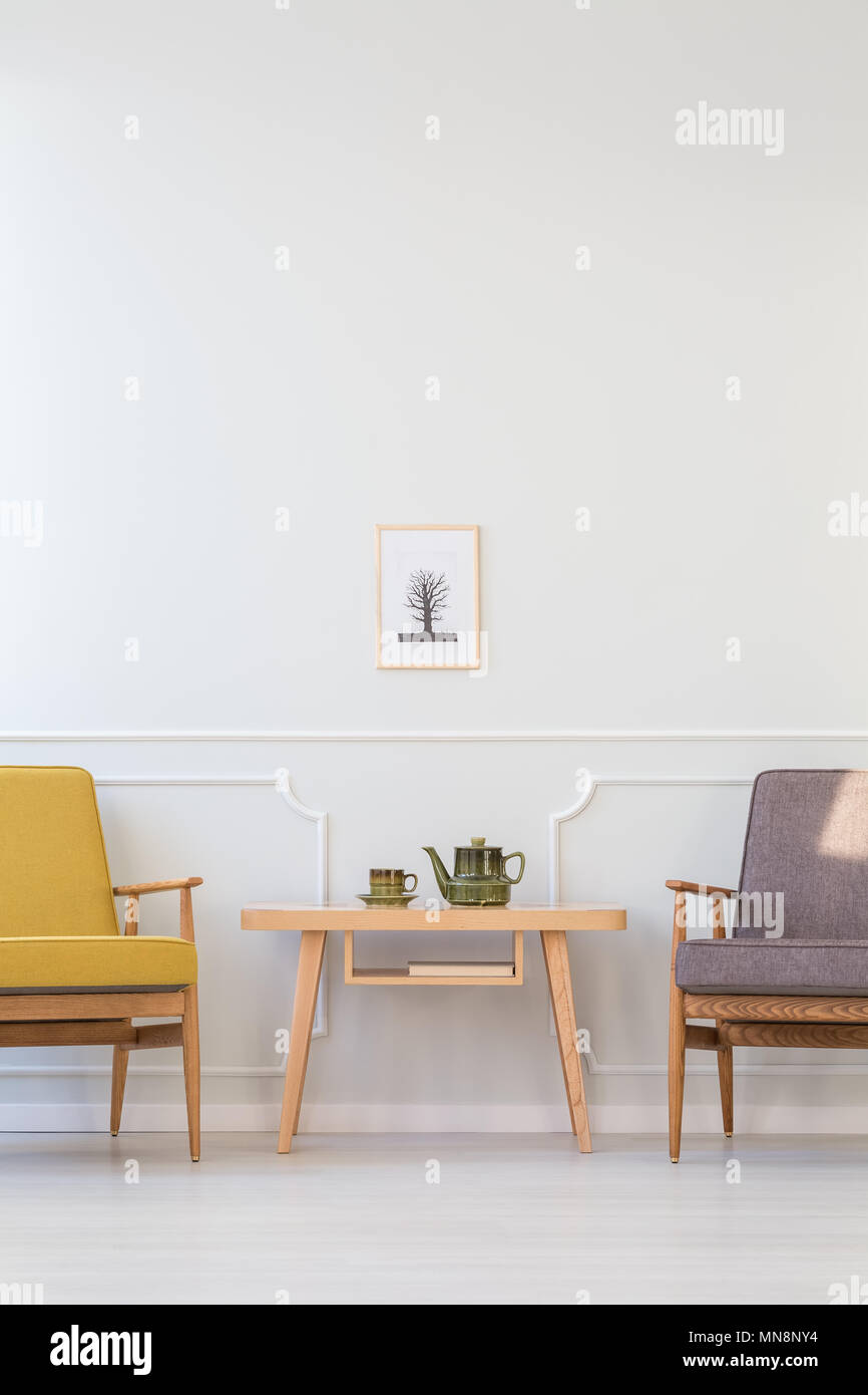 Wooden table between grey and yellow armchair against white wall with