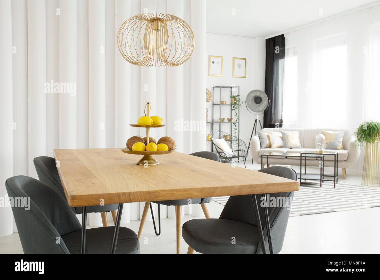 Bright dining room interior with fruit on wooden table, gray chairs and  tubes wall. Living room in the background Stock Photo - Alamy