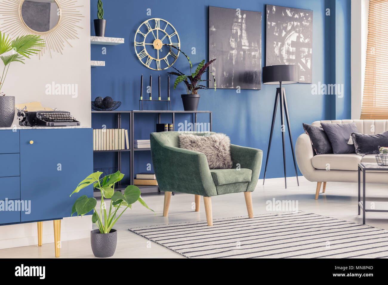 Retro typewriter and golden wall clock in a blue living room interior with paintings and modern furniture Stock Photo