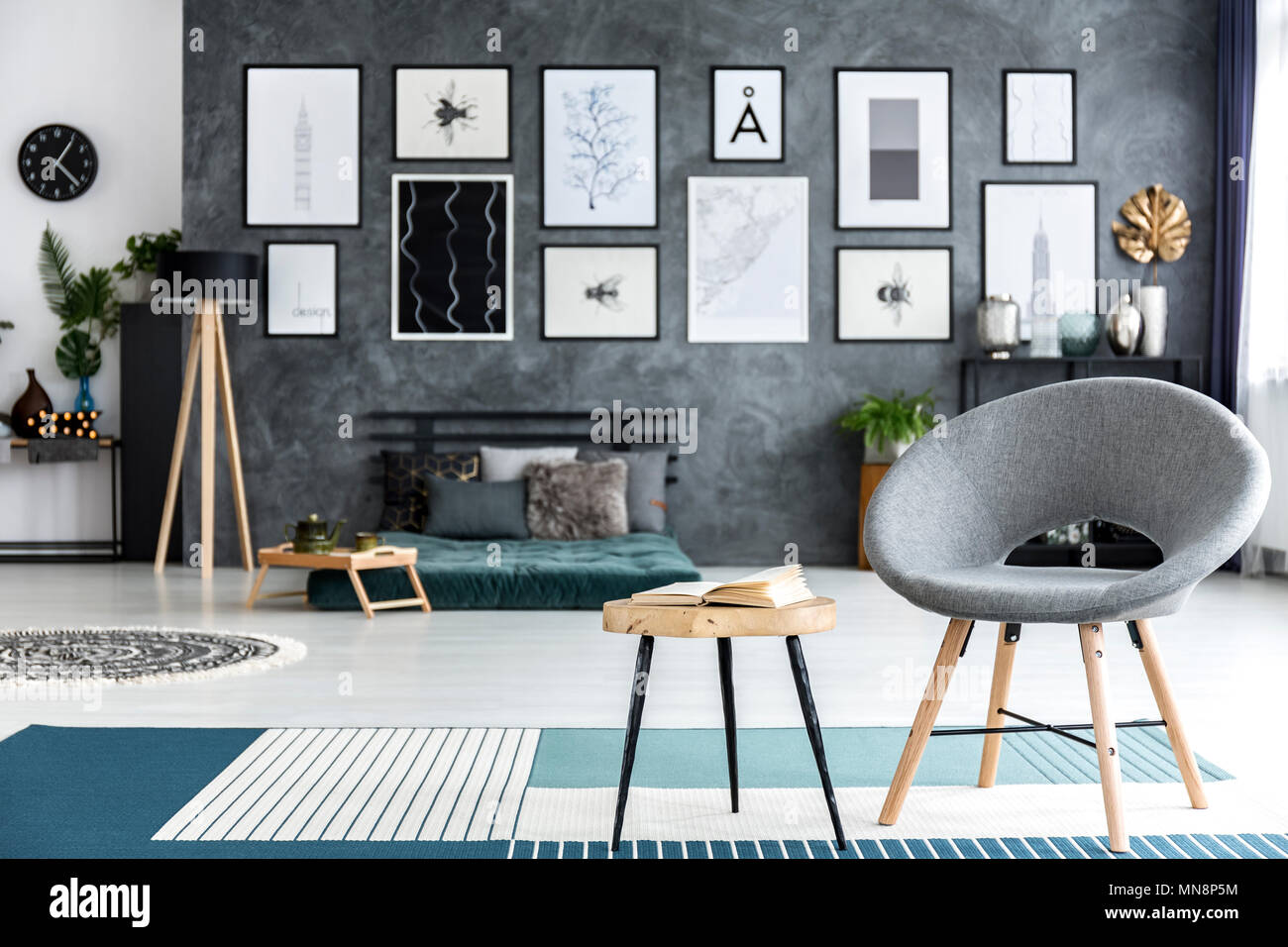 Close up of grey armchair next to a wooden table with book on blue carpet in bedroom interior