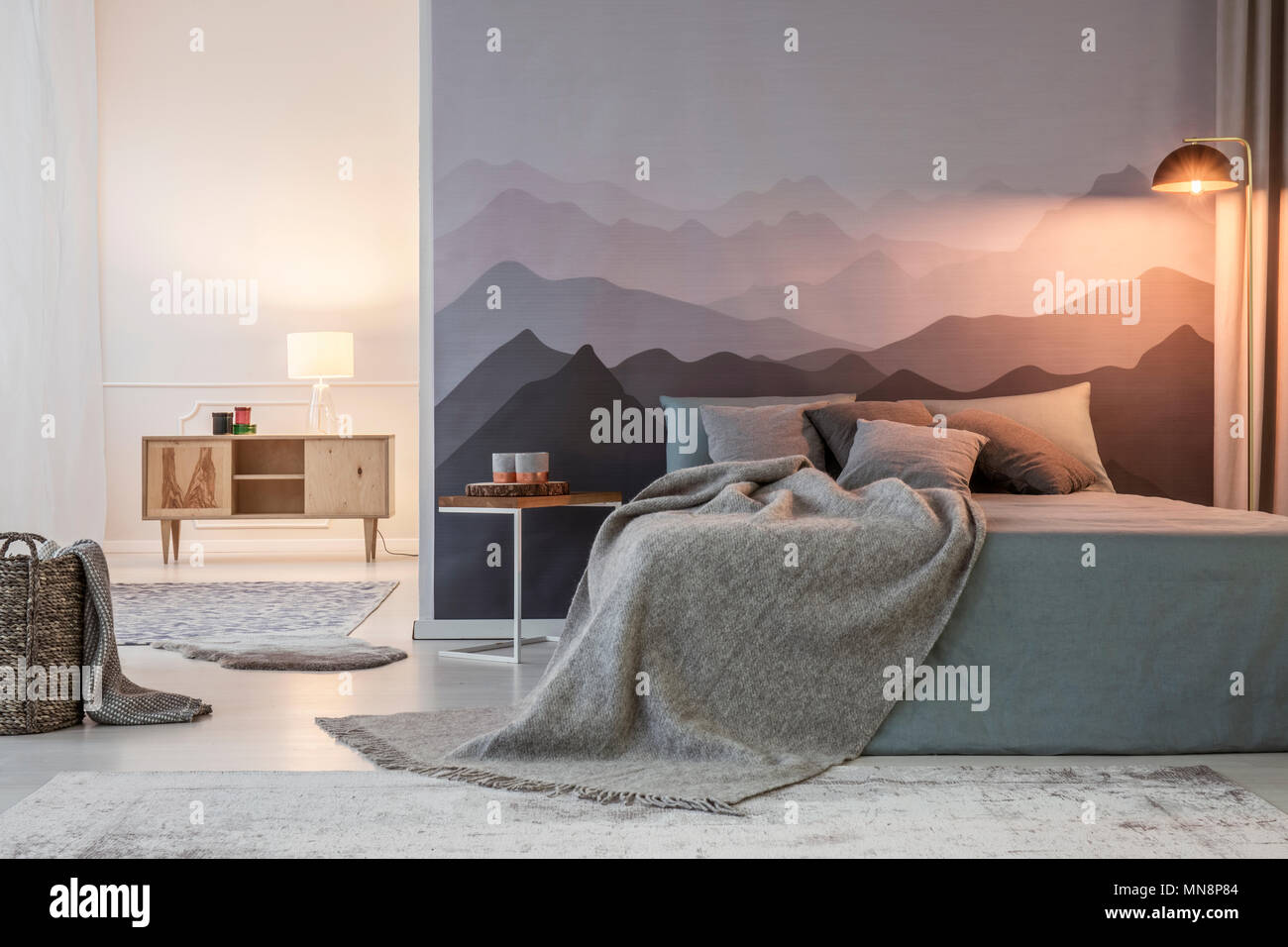 Grey blanket on bed against mountain wallpaper next to a stool with light in bedroom interior Stock Photo Alamy