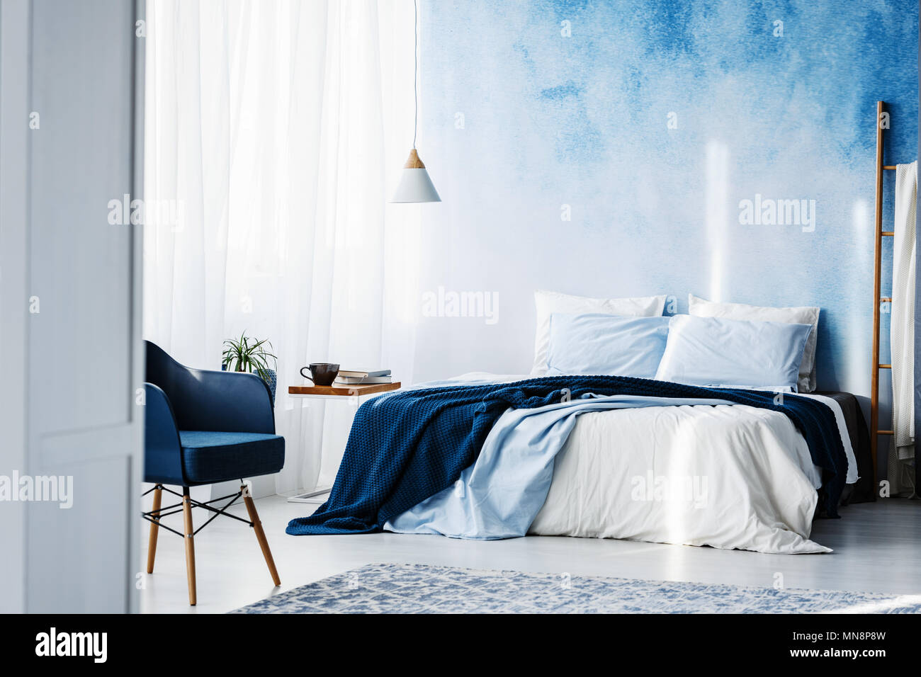 Navy blue armchair and king size bed with blankets and pillows in a