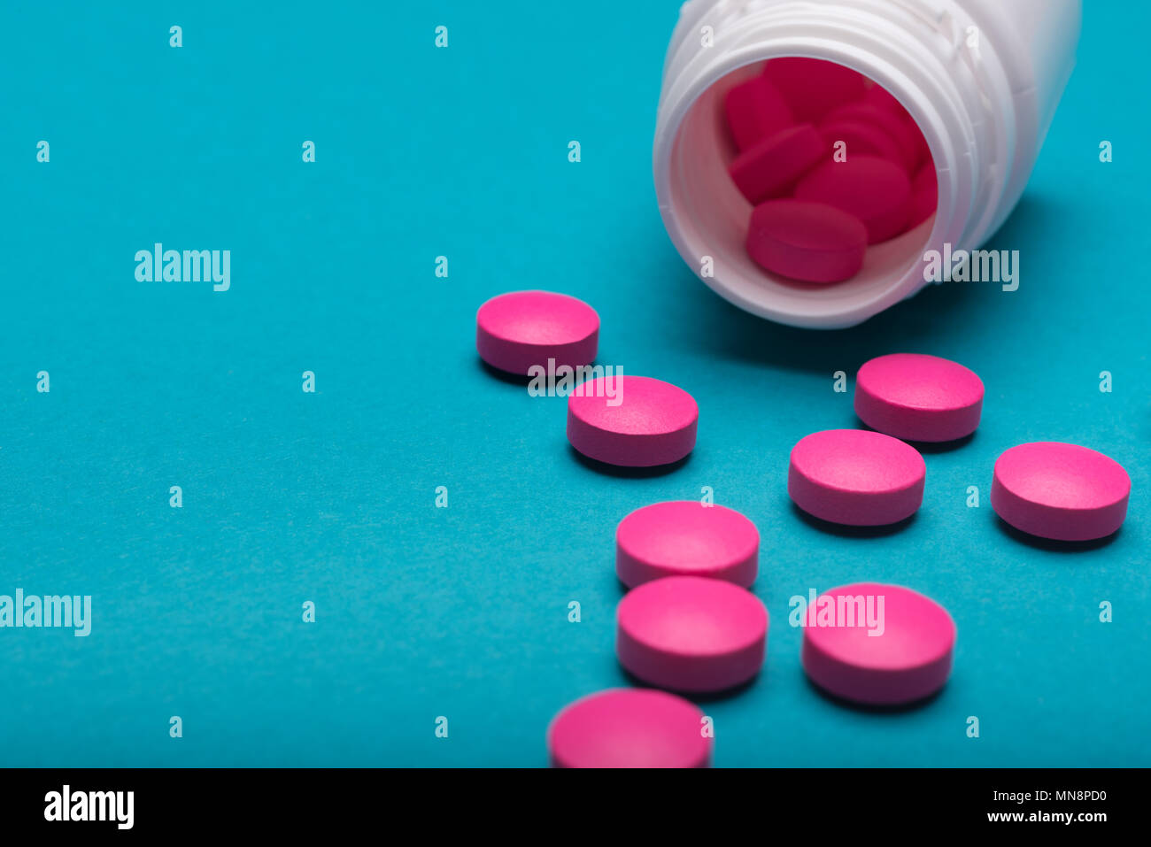 Medication bottle and bright pink pills spilled on dark blue coloured