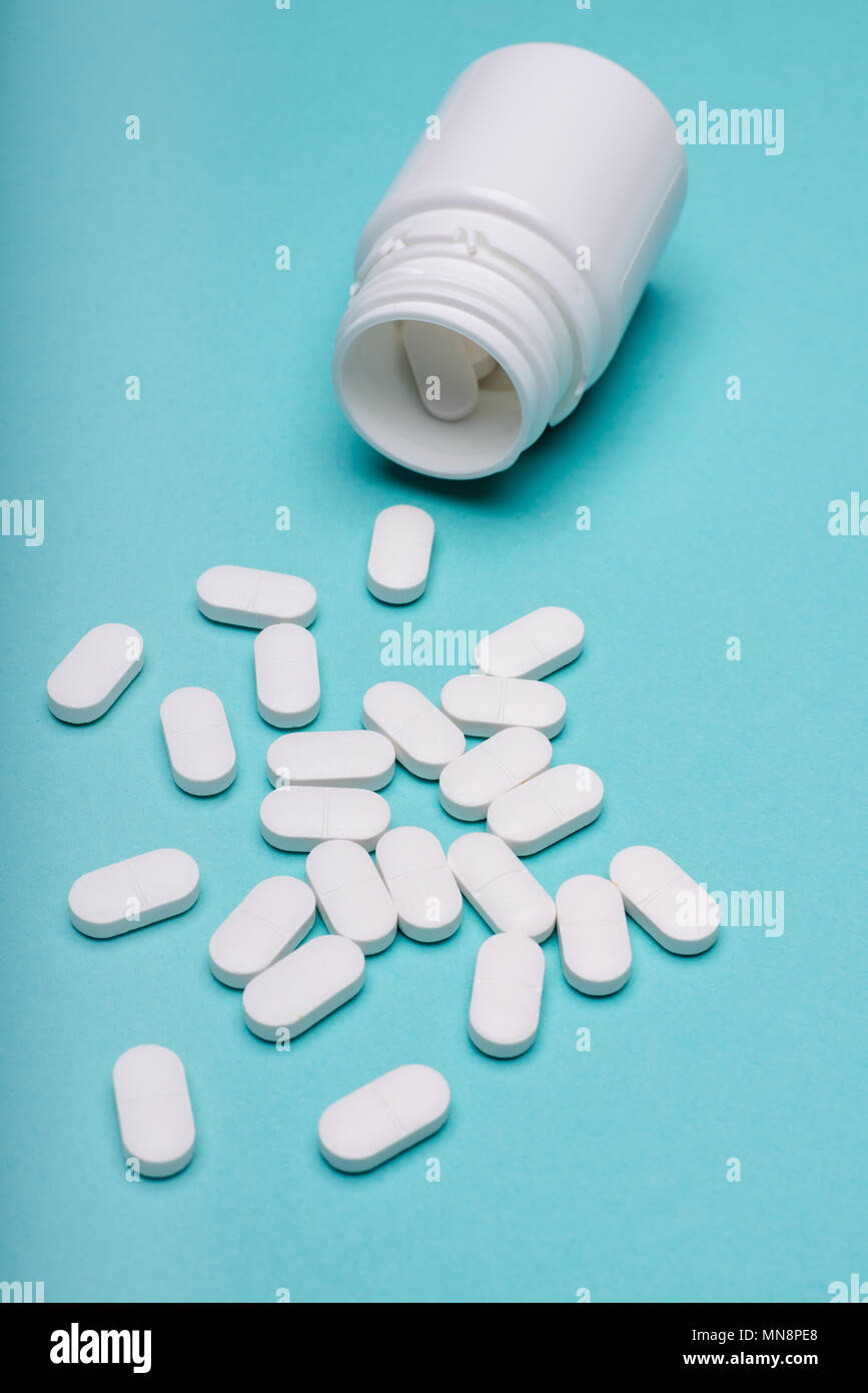 Medication bottle and white pills spilled on blue pastel coloured background. Medication and prescription pills flat lay background. Stock Photo