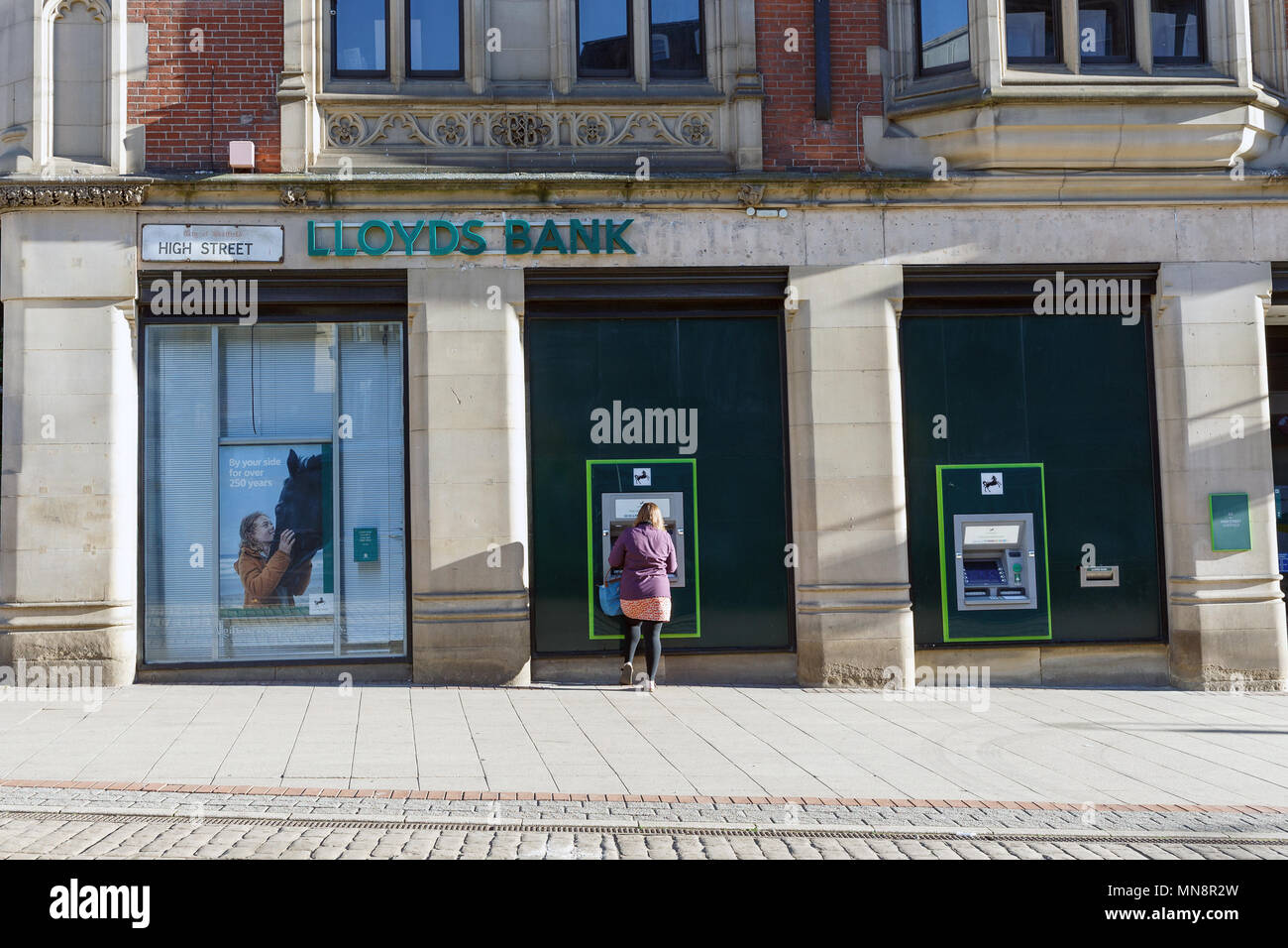 A woman using an ATM at a Lloyds Bank in the United Kingdom. Stock Photo