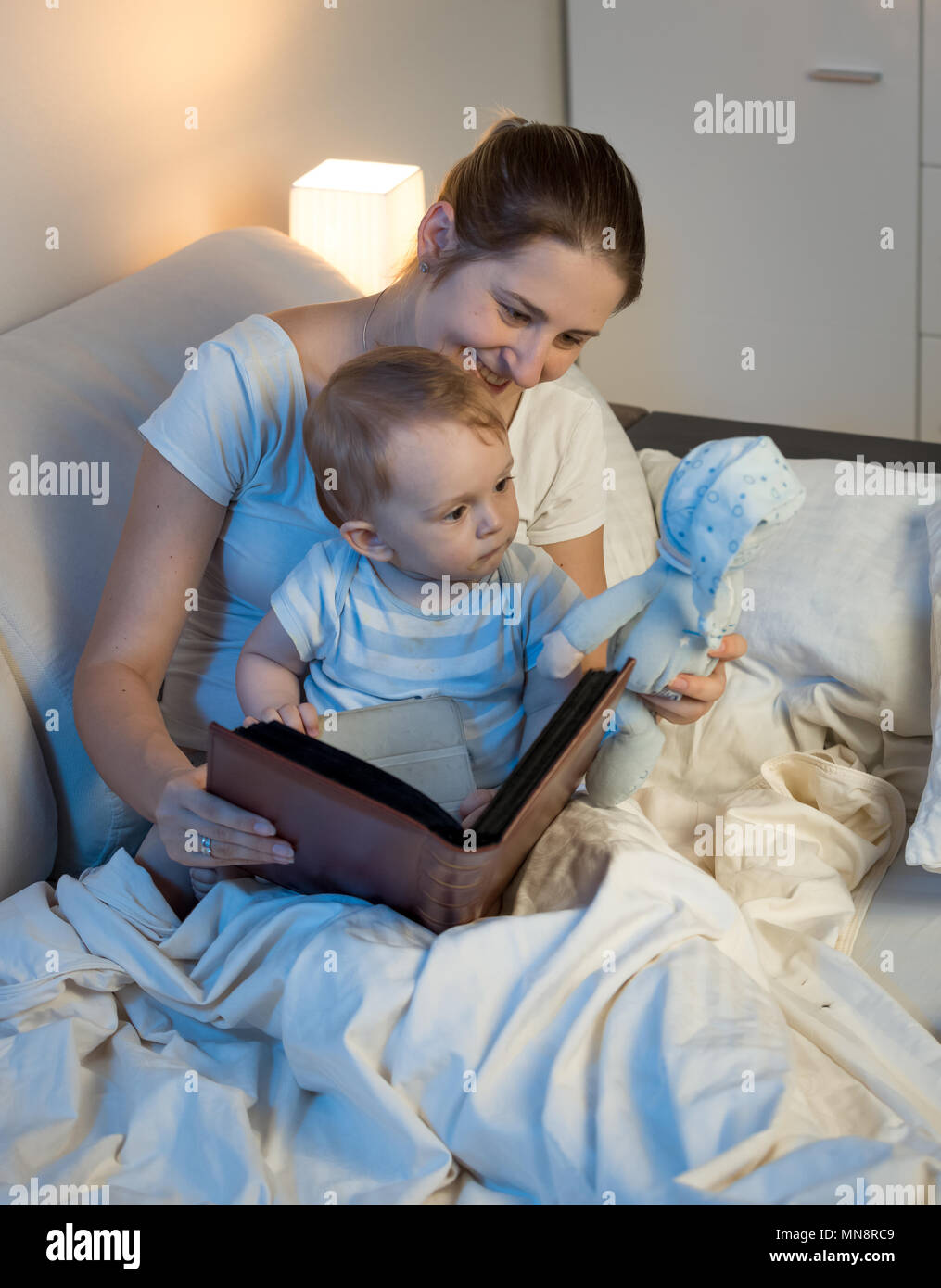 Portrait of young mother with baby boy reading book before going to