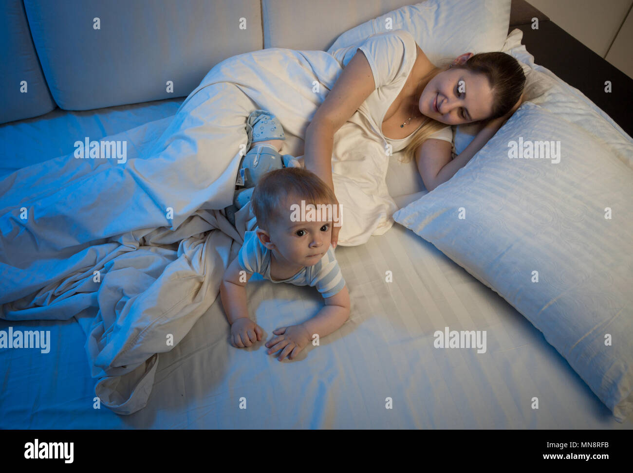 Young mother with her baby son lying on bed at night Stock Photo