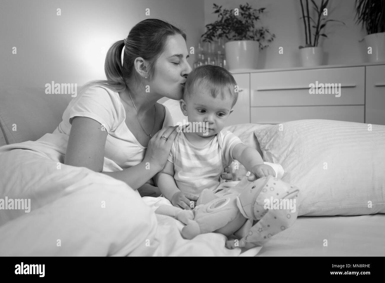Black and white portrait of young mother kissing her baby son before going to sleep Stock Photo