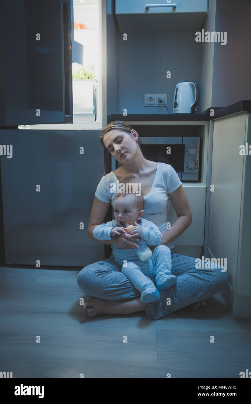 Young tired mother fell asleep while feeding her baby boy with milk at