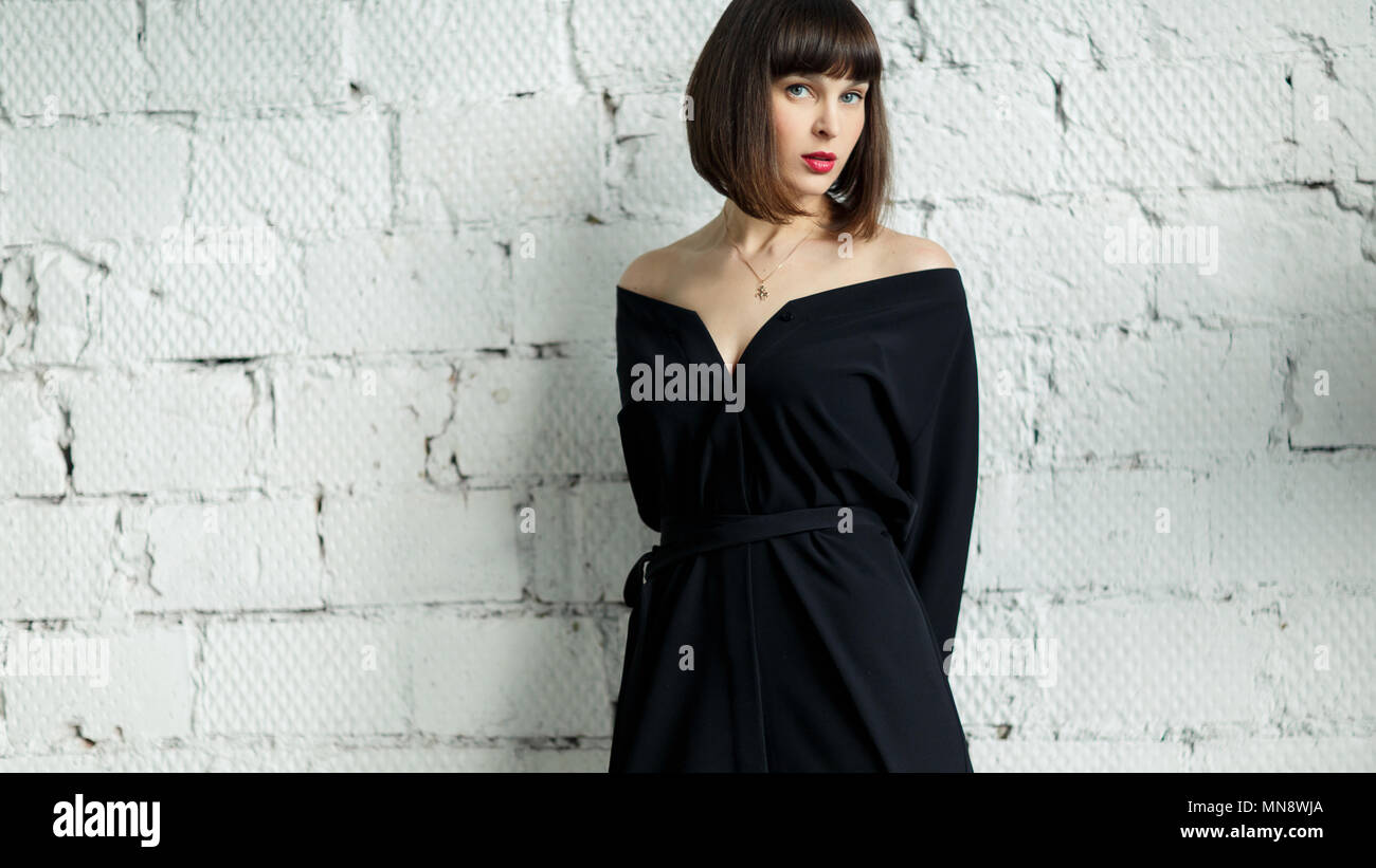 Photo of young brunette in black dress against white brick wall Stock Photo