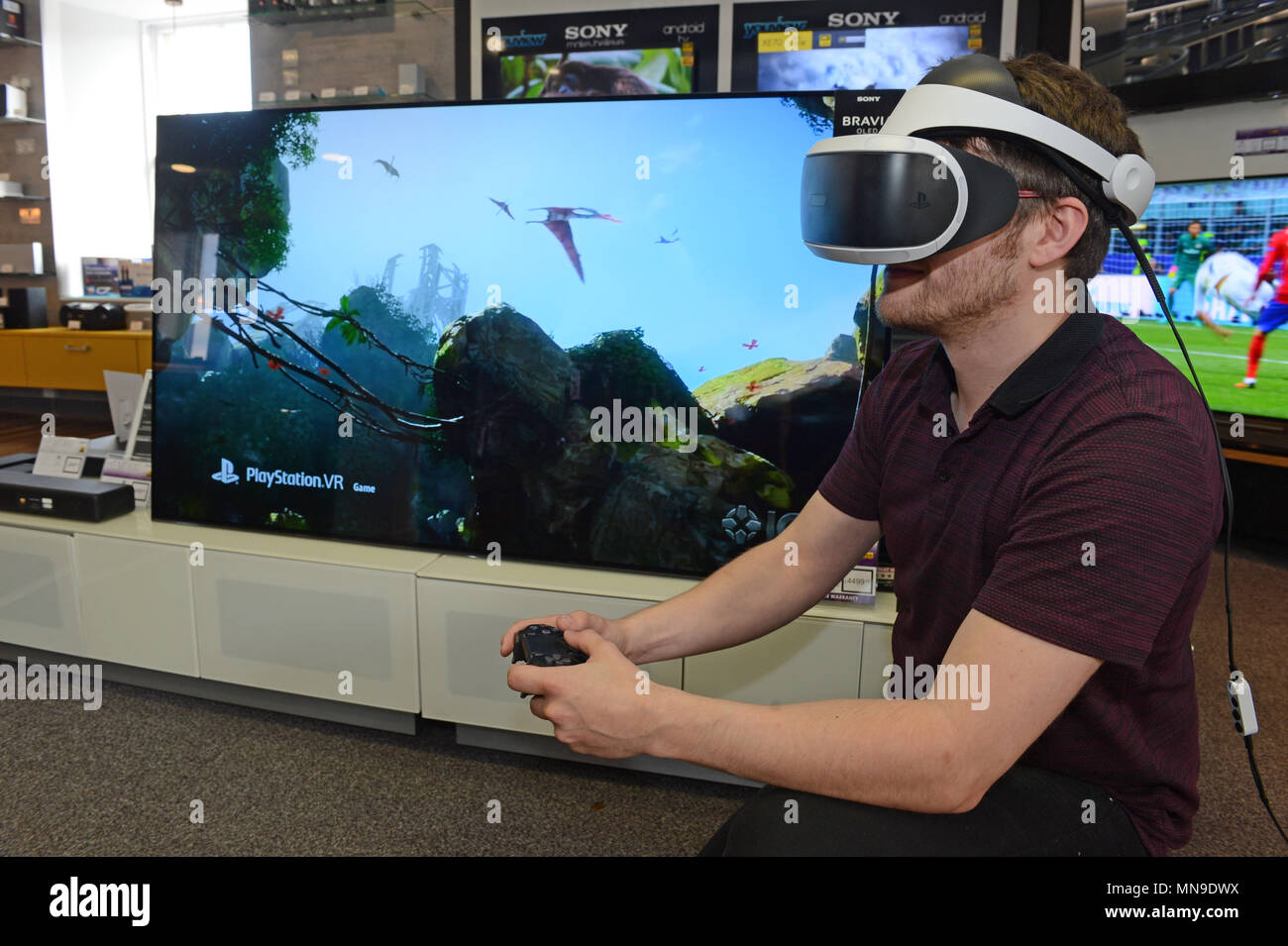 Man in retail store wearing a Sony VR headset with playstation controller  and game on Sony TV Stock Photo - Alamy