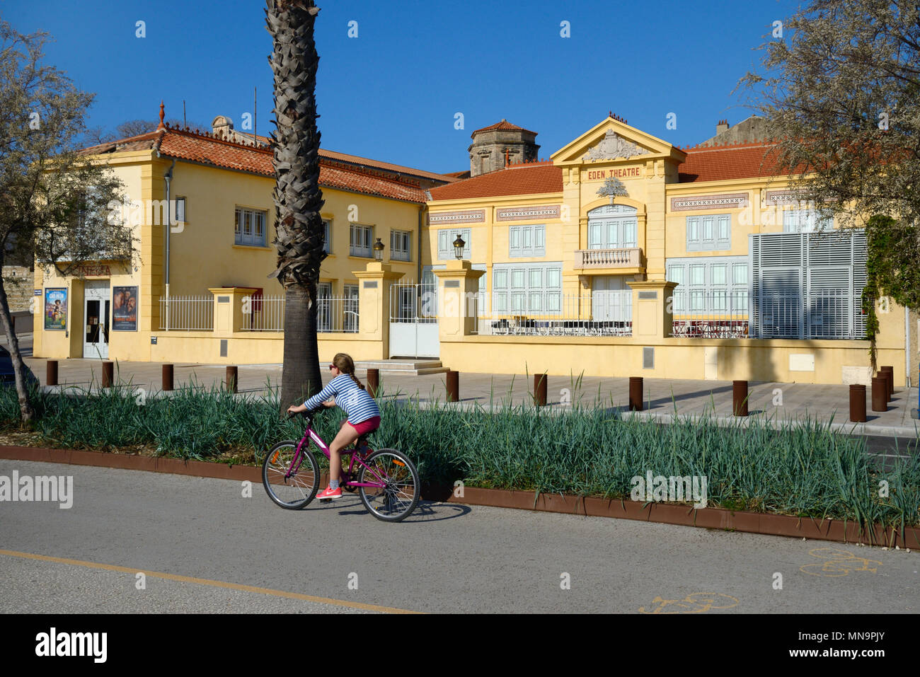 Girl Cycling in Cycle Lane Past the Historic Eden Theatre or Eden Theater, one of the world's earliest cinema or movie theatre, La Ciotat, France Stock Photo