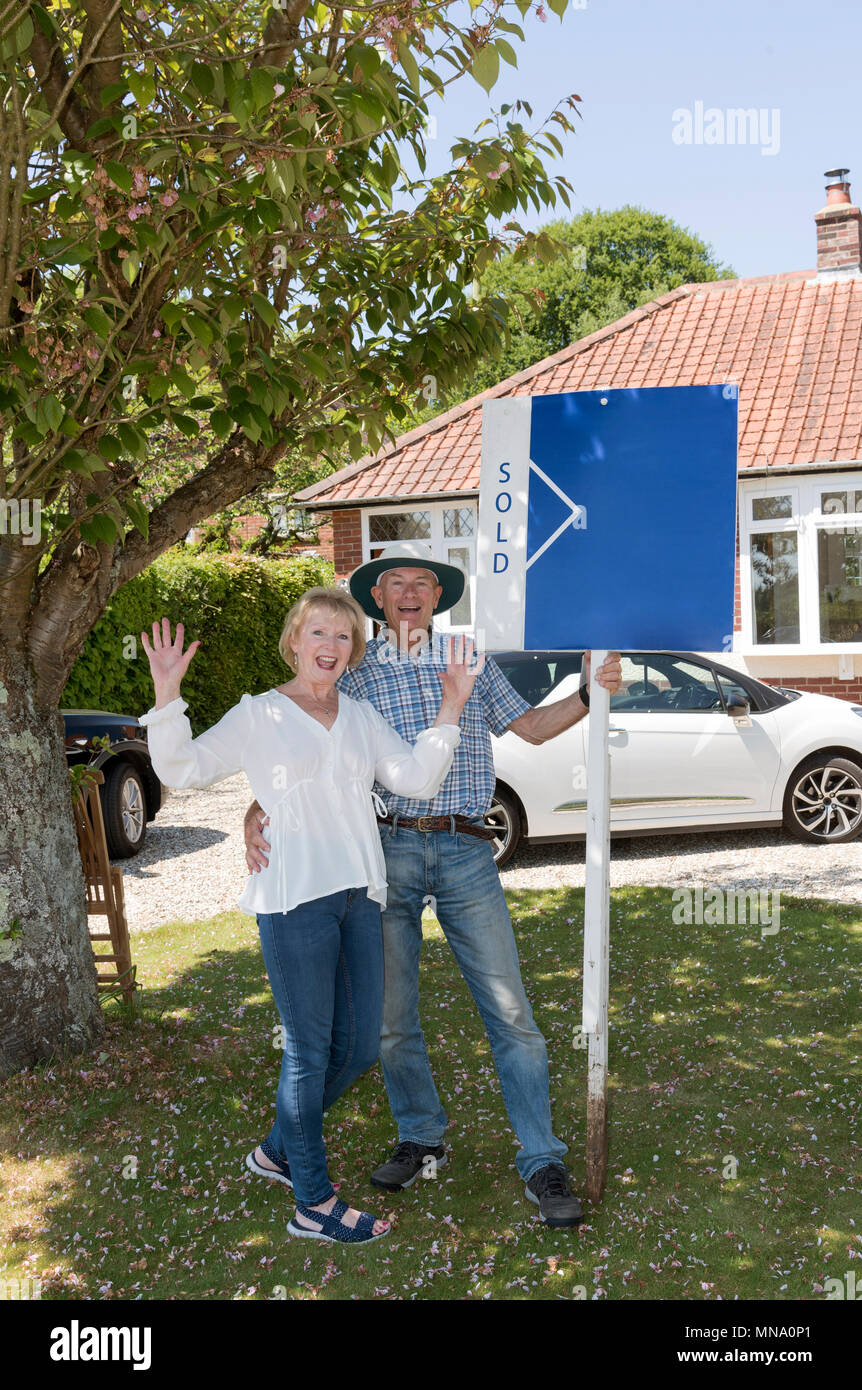 Couple standing with a sold sign outside their home Stock Photo - Alamy
