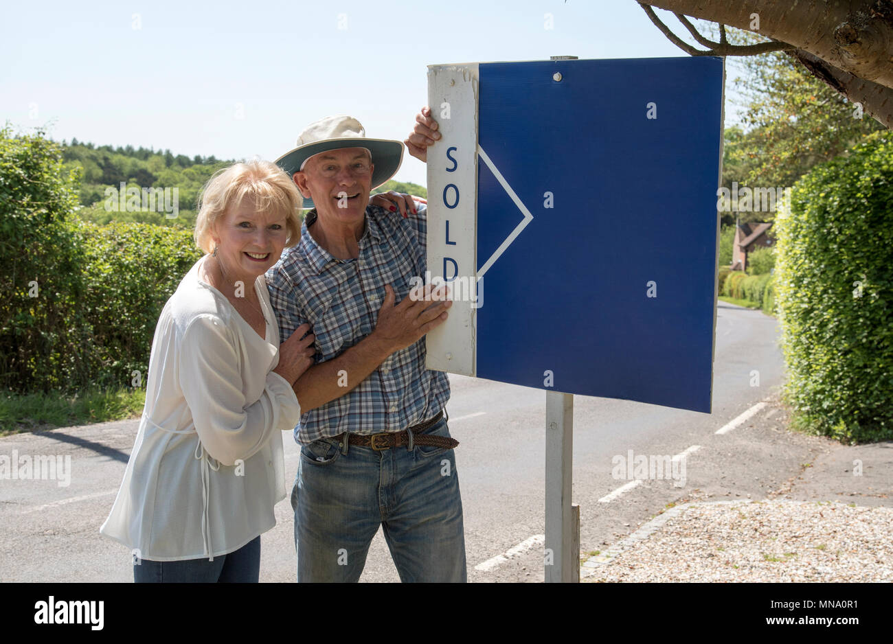 Couple standing with a sold sign outside their home Stock Photo - Alamy