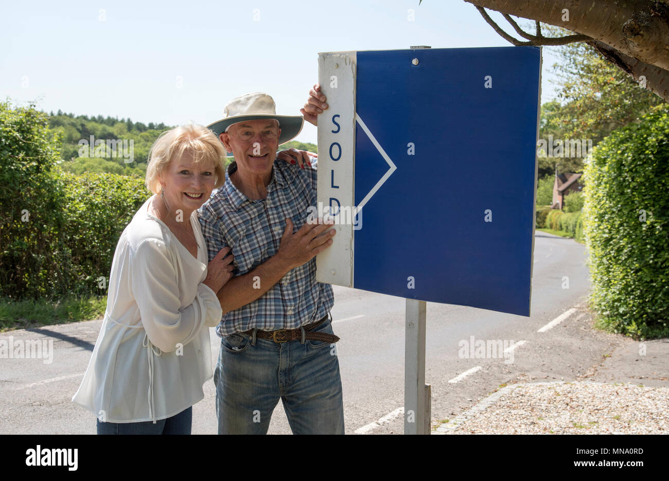 Couple standing with a sold sign outside their home Stock Photo - Alamy