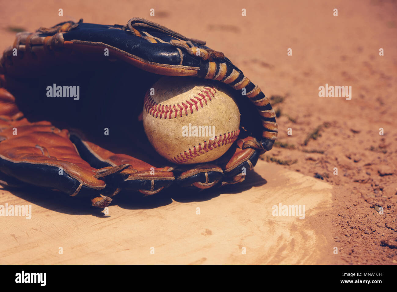 Vintage baseball in players glove laying on homeplate, ball field dirt