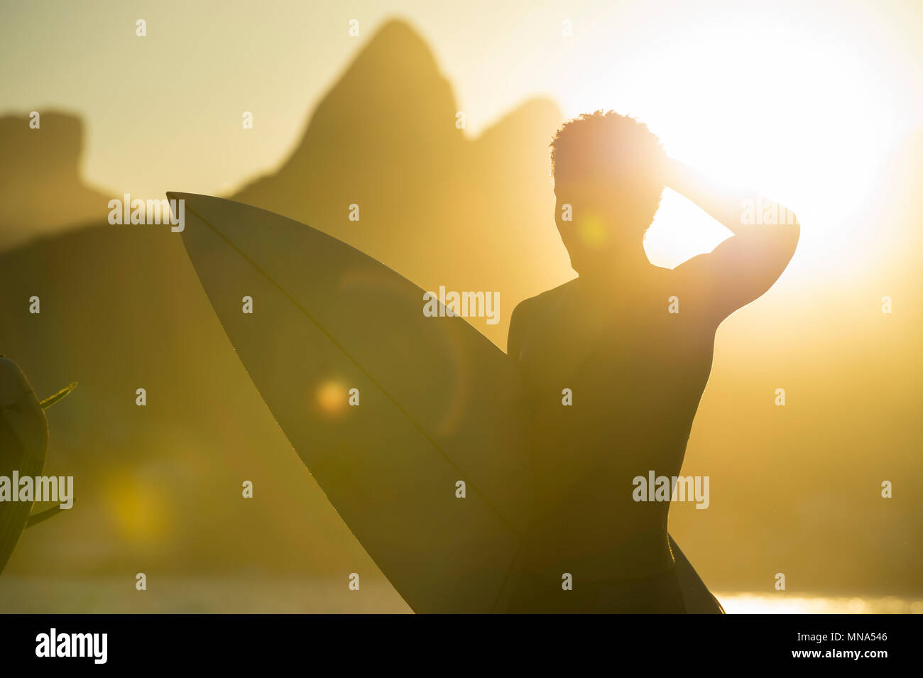 RIO DE JANEIRO - MARCH 20, 2017: Sunset silhouette of young surfer with surfboard at Arpoador with two brothers mountains in the background in Ipanema Stock Photo