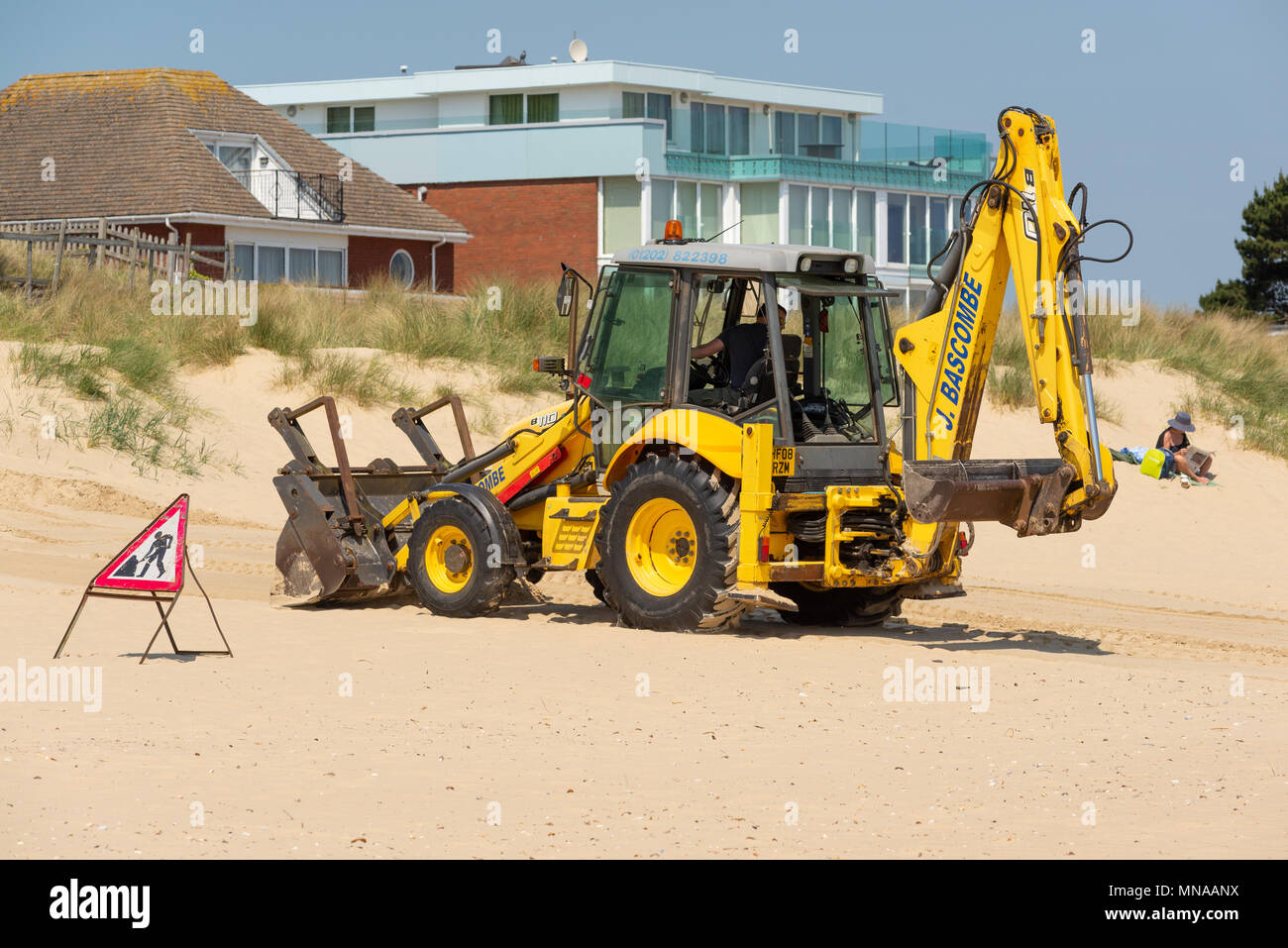 JCB digger performing sand levelling manoeuvres on the beach at Sandbanks, Poole, Dorset, UK Stock Photo
