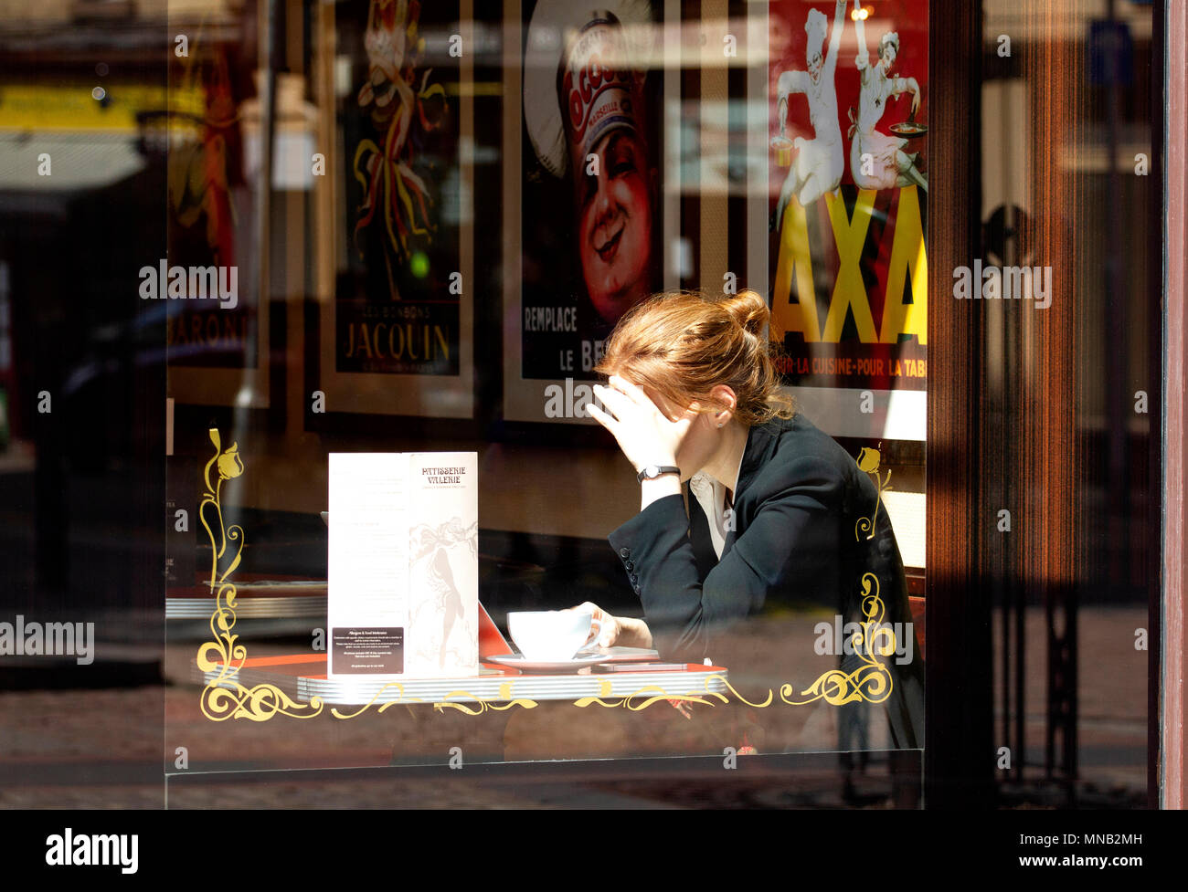 A young blonde woman sitting inside the Cordially Cake Cafe using her laptop and enjoying a cup of coffee in Dundee city centre, UK Stock Photo