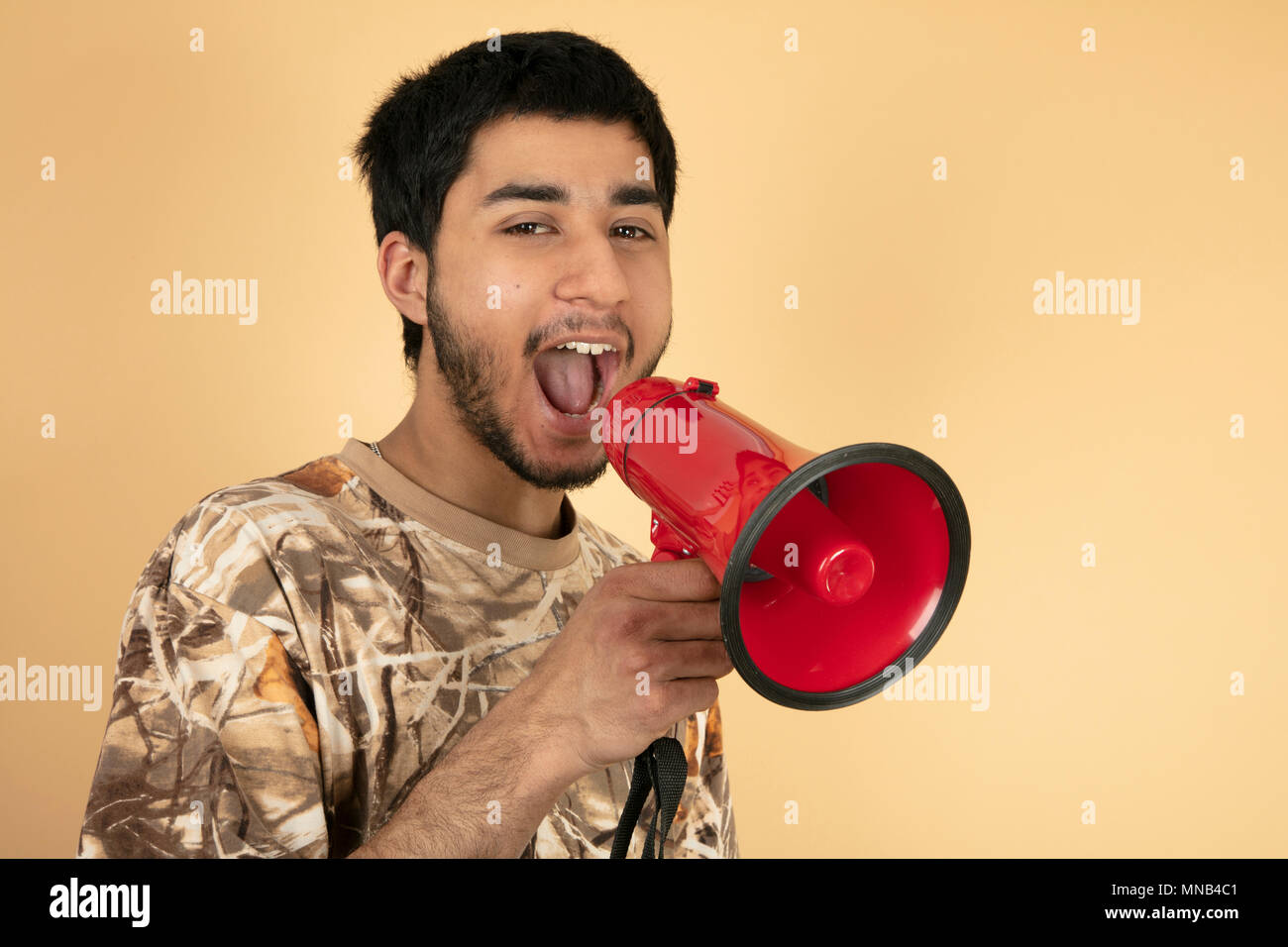 Young Man shouting in speaker on beige background Stock Photo