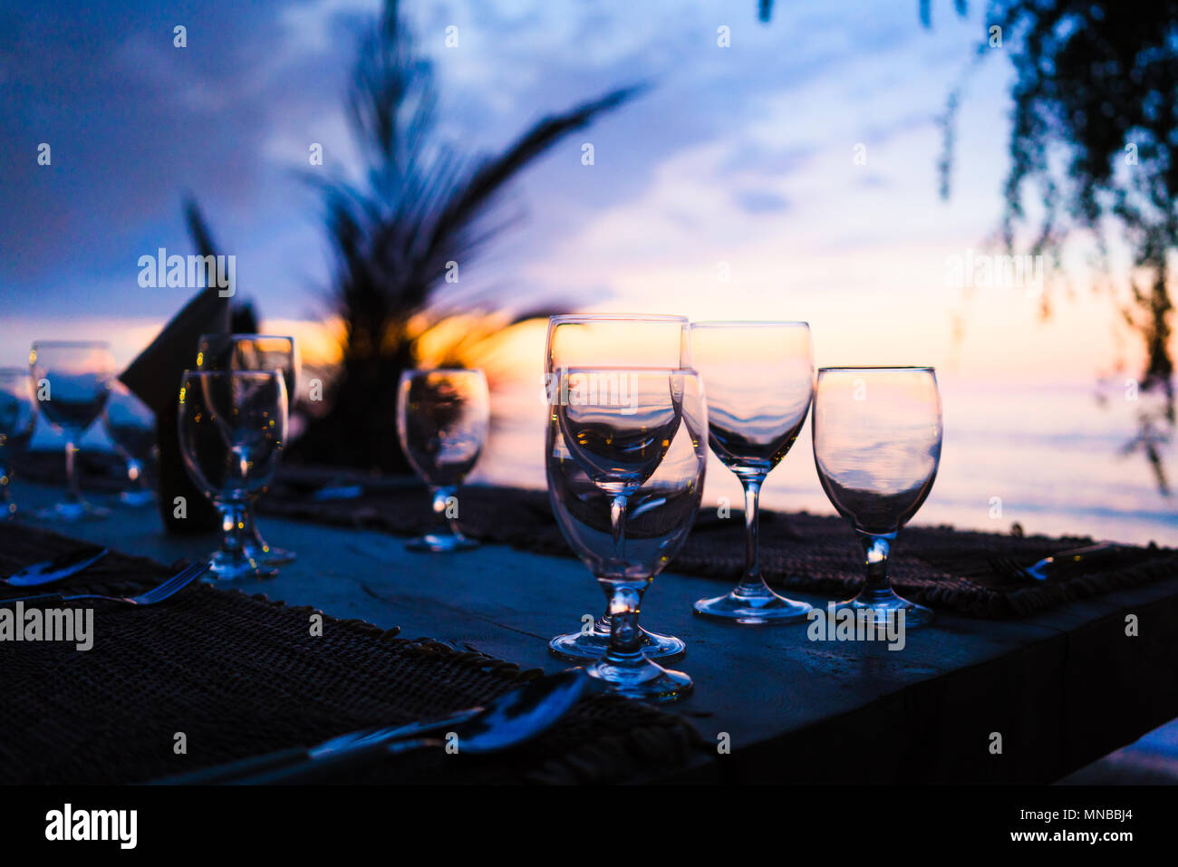 Glasses on table in tropical restaurant at sunset Stock Photo