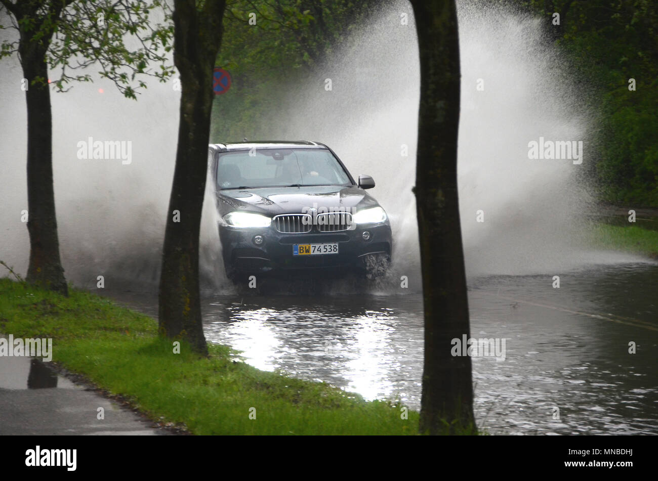 Sonderborg, Denmark - May 10, 2018:  A car splashes trough water on a road that is flooded afther a heavy rainfall. . Stock Photo
