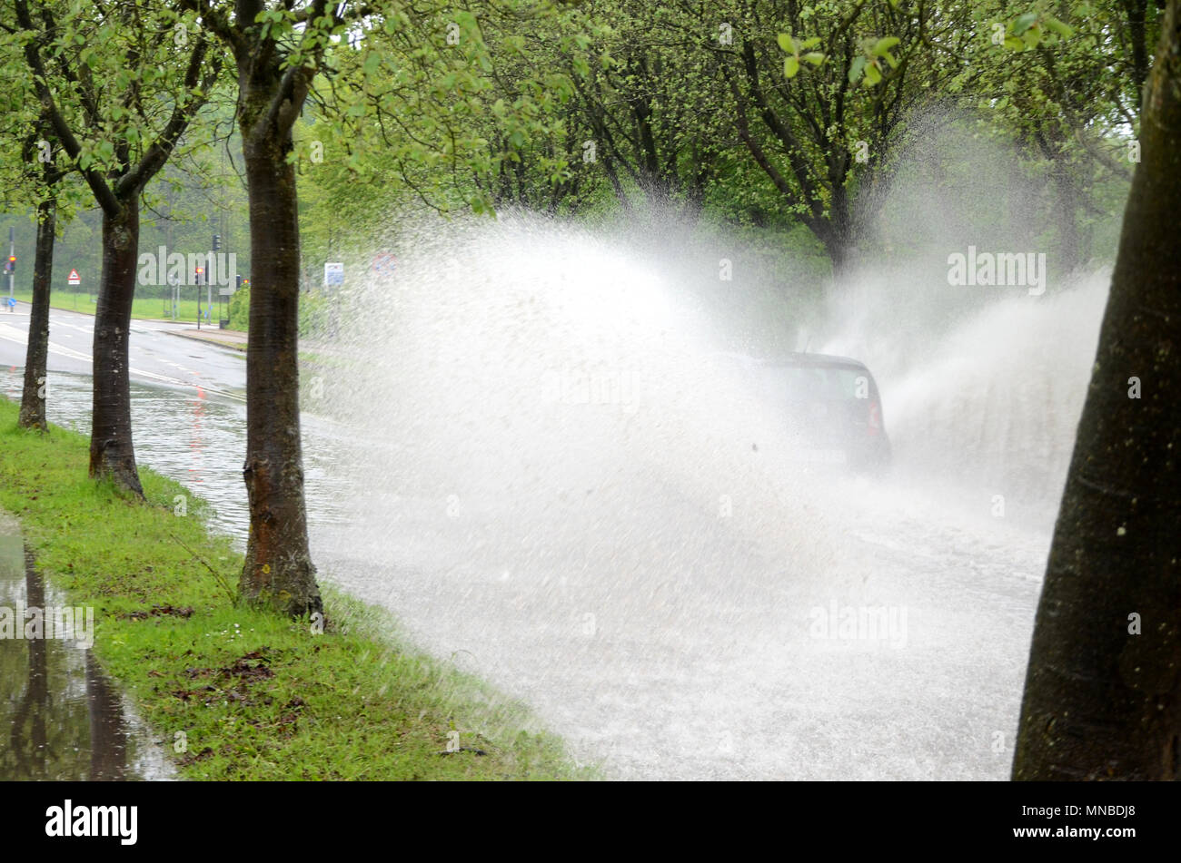 A car hidden in a large splash drives on a road that i flooded because of severe rainfall and bad kept drains. Stock Photo