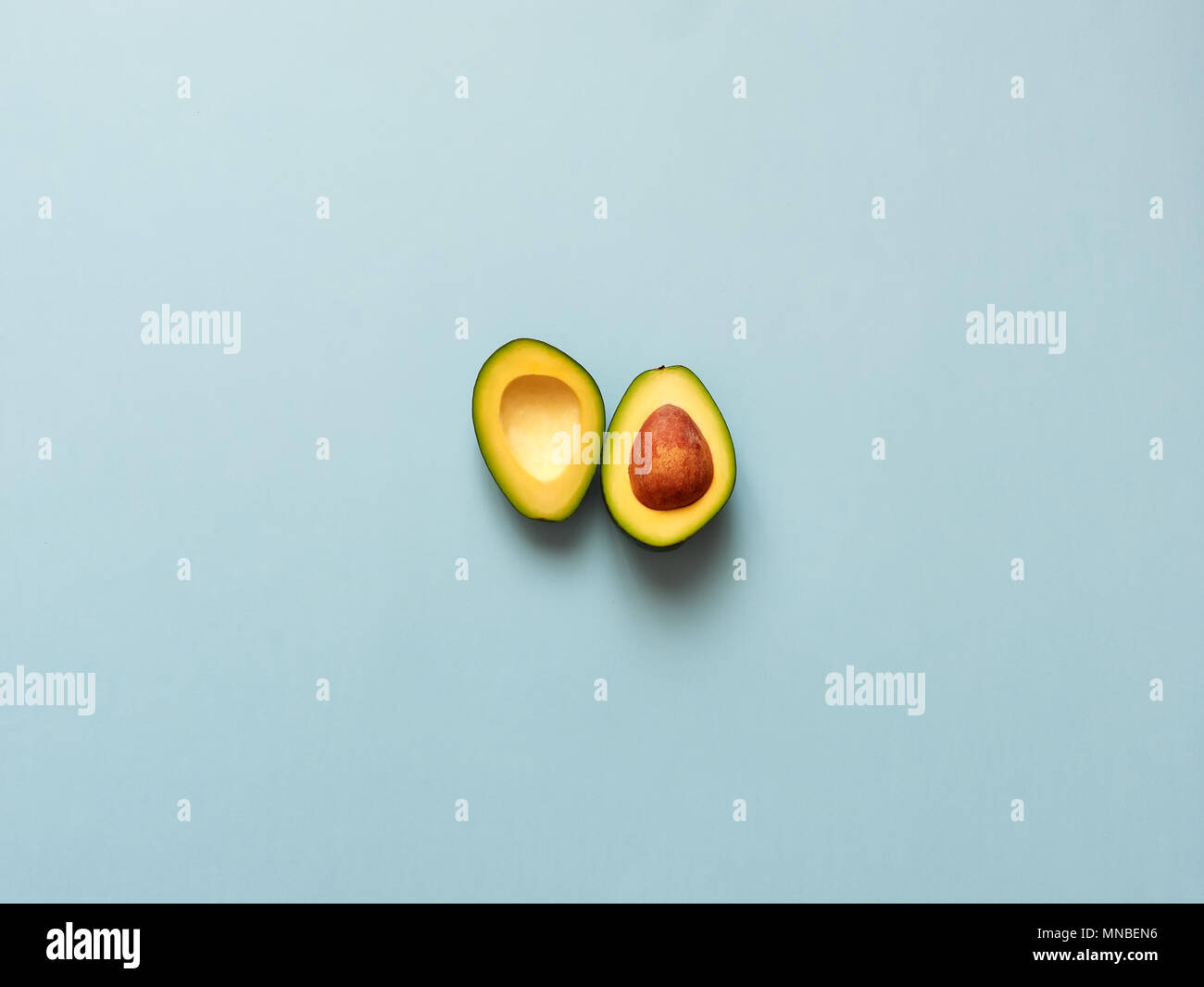 Avocado sliced with seed isolated in blue background viewed from above - flatlay look Stock Photo