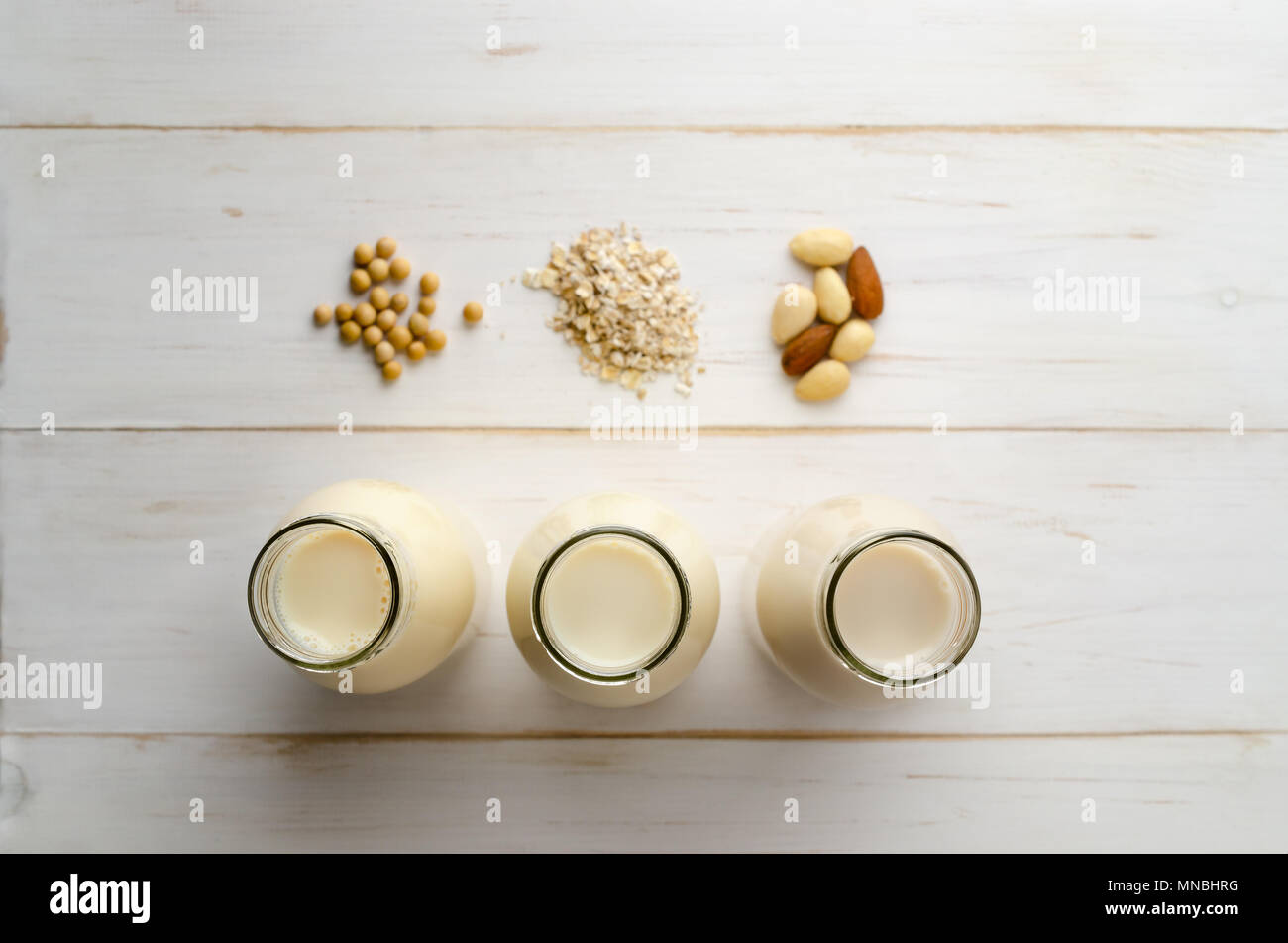 Overhead shot of soya, oat and almond milk drinks in a row of open bottles with ingredients on painted white, wood planked table. Shallow depth of fie Stock Photo
