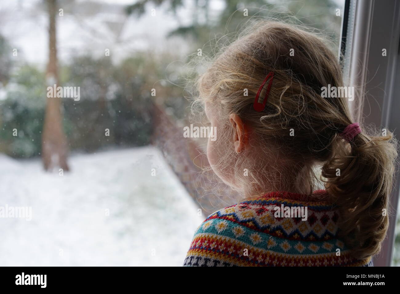 Little girl looking out through the window onto a snow-covered garden in Cornwall, England Stock Photo