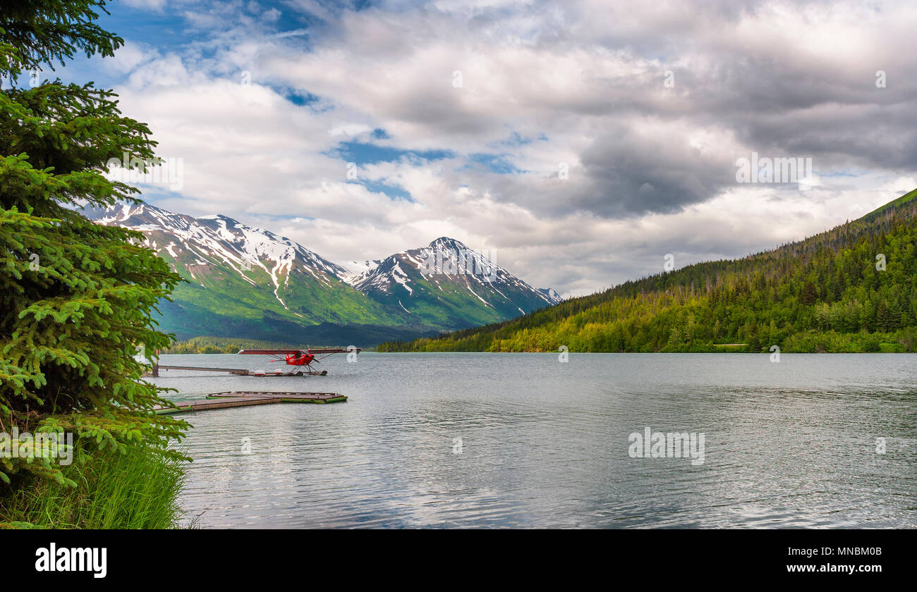 A float plane docked on Moose Lake in Alaska, with the Chugach mountain range in the background under cloudy skies. Stock Photo